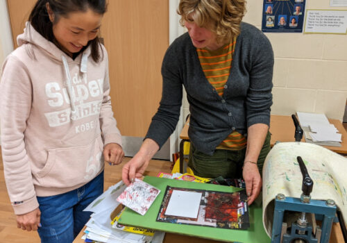 Artist Jac Campbell demonstrates a small printing press to a workshop participant.