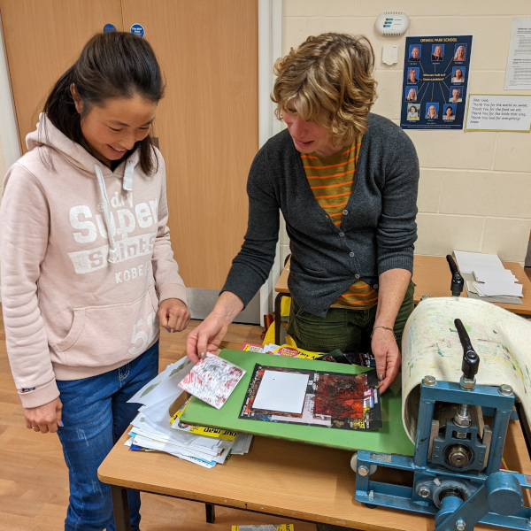 Artist Jac Campbell demonstrates a small printing press to a workshop participant.