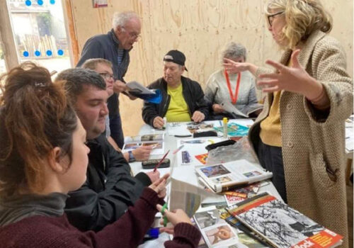 Brave artists and staff work together around a table, studying books and art works,