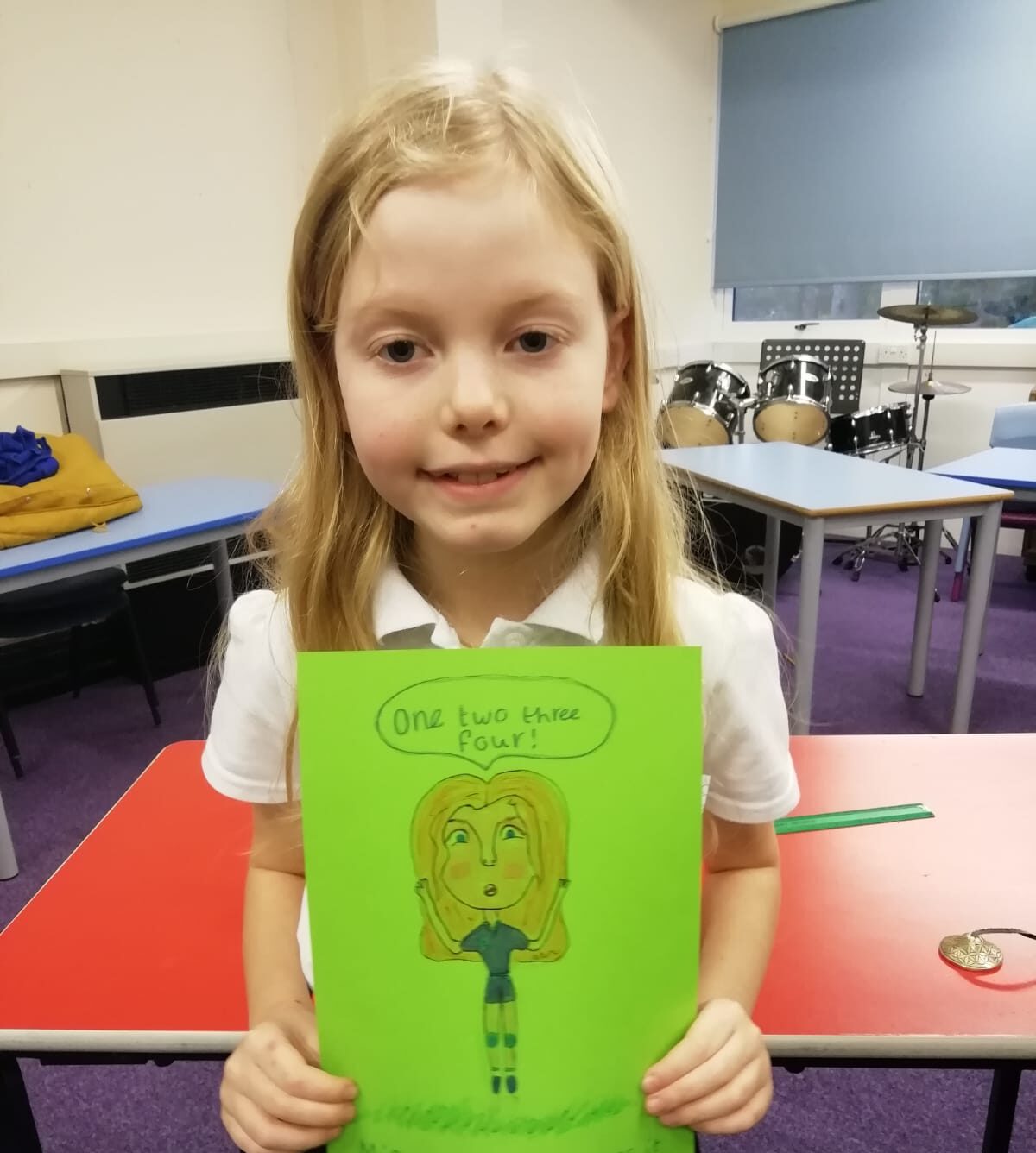 A school girl with long blonde hair holds up a cartoon of herself, dressed in blue football kit and calling out 1,2,3,4