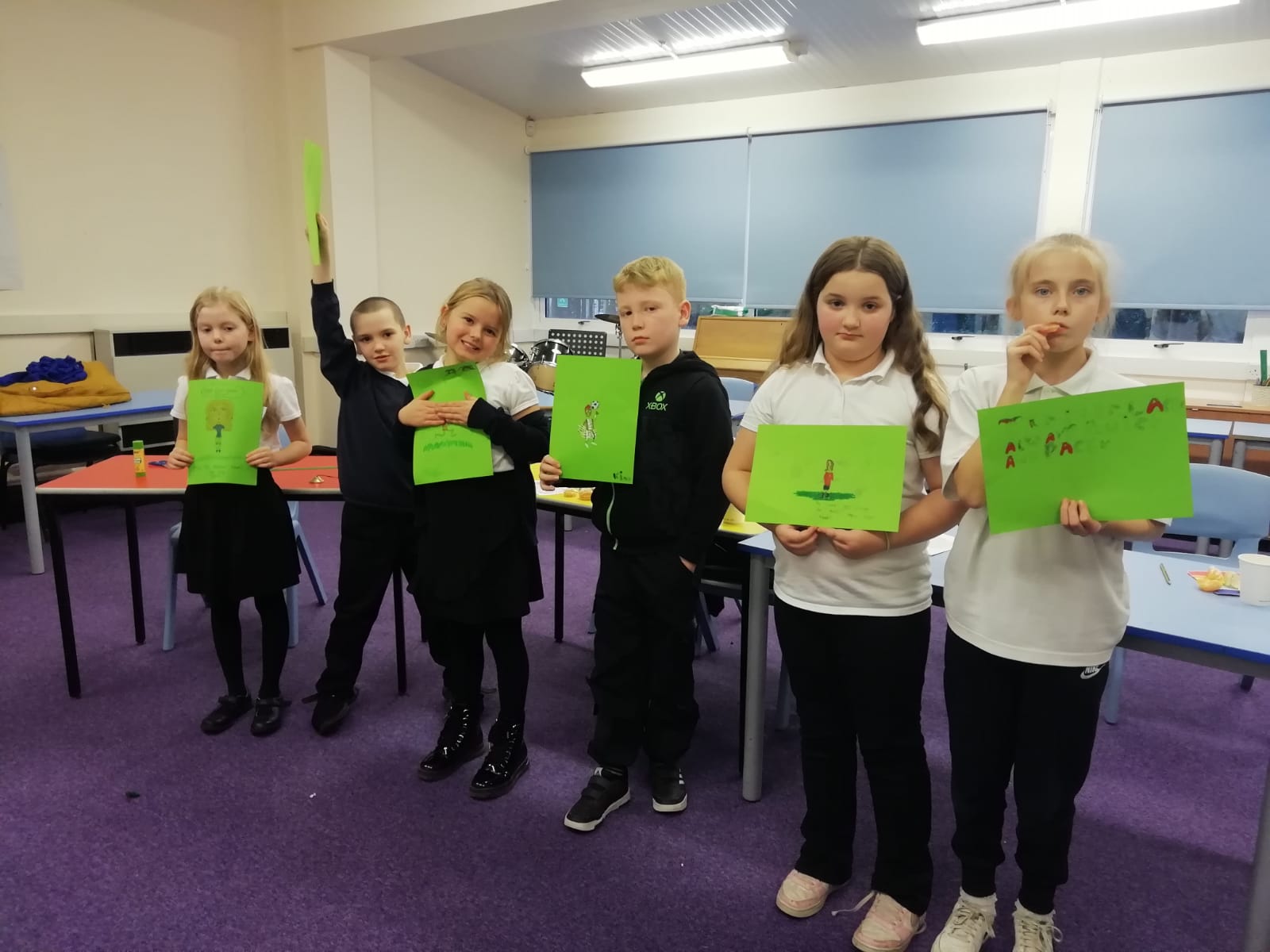 A row of 6 school children holding up cartoons they have drawn of themselves in football kit