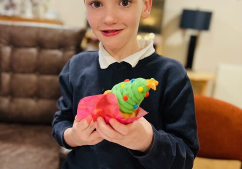 A young school boy holding a cupcake with icing like a Christmas tree on top