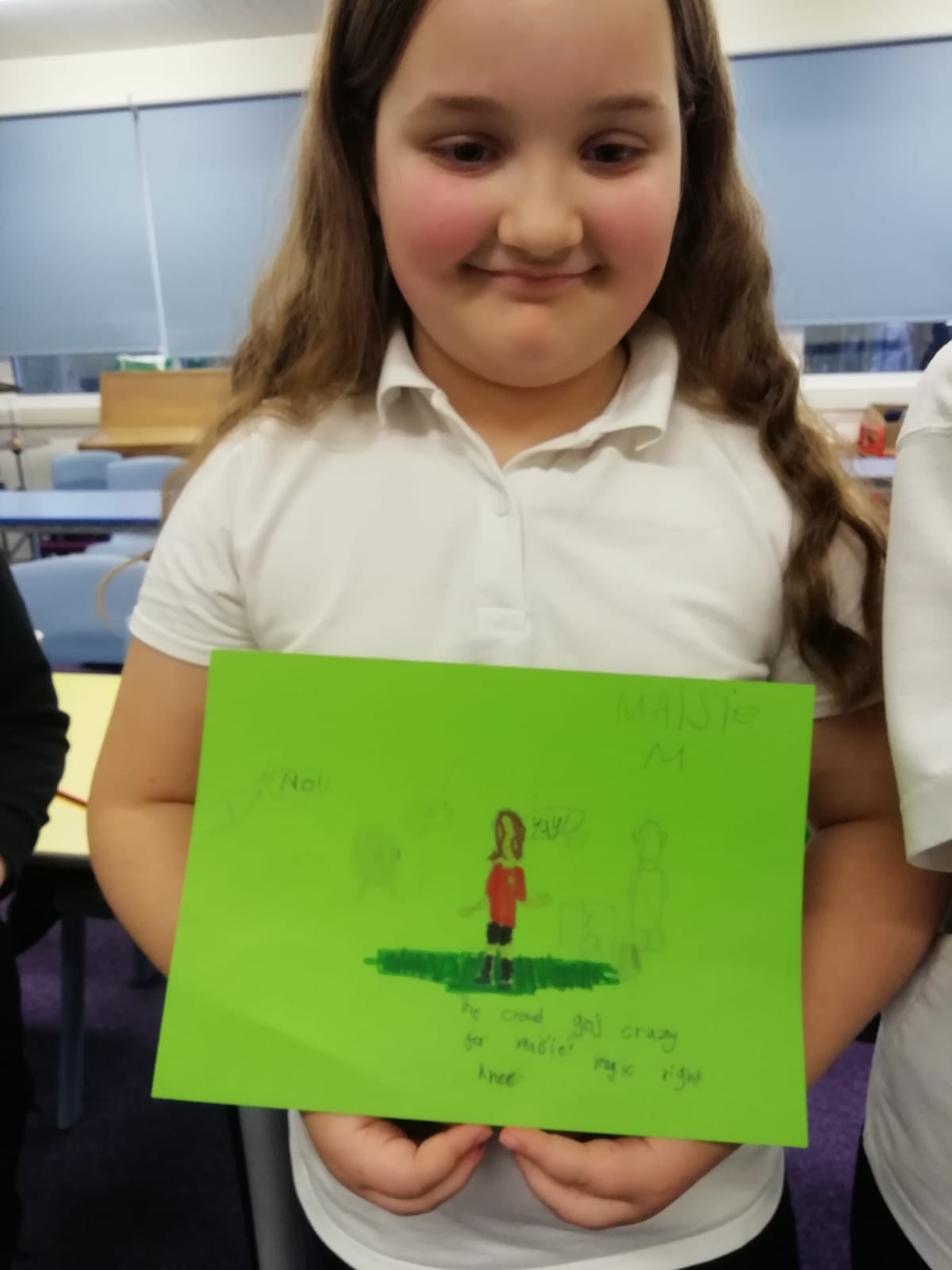 A school girl wearing a white T-shirt stands holding a cartoon of herself that she has drawn