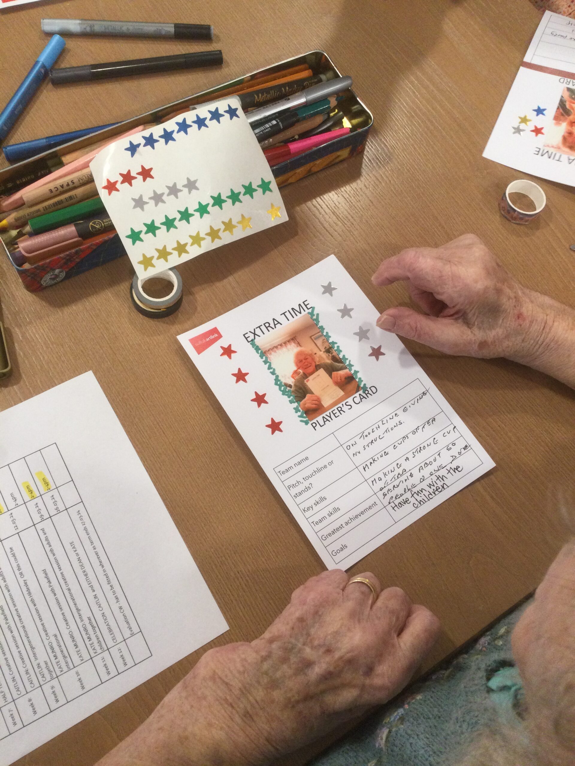 An overhead view of a table with craft materials and someone working on a card with a photo of themselves top centre