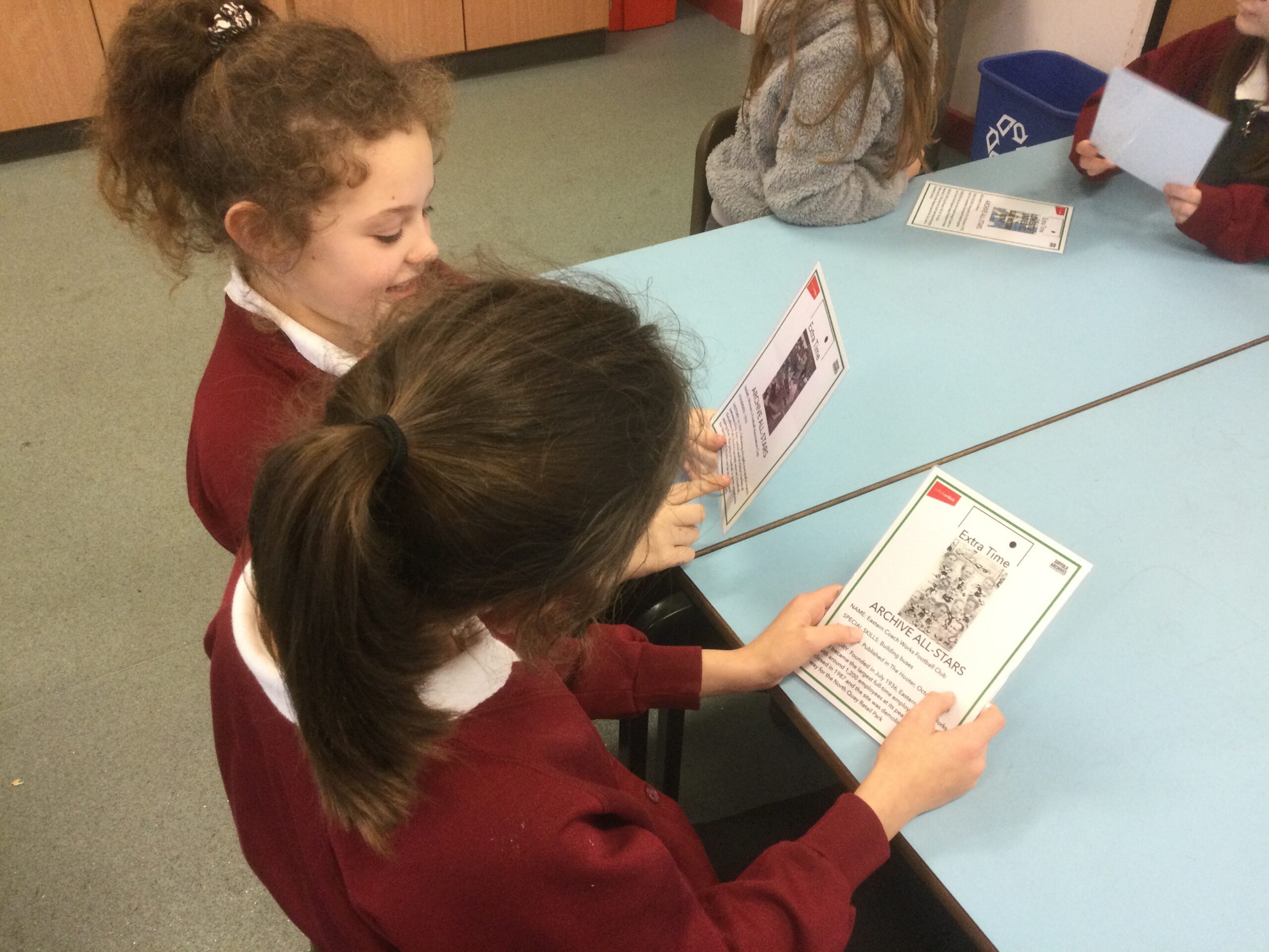 Two school girls studying laminated cards showing details about Lowestoft football clubs