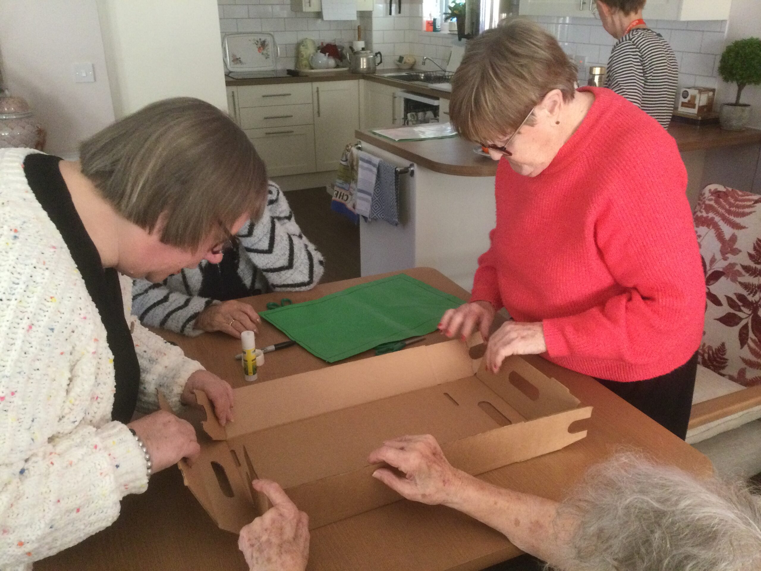 Two women standing at a table, constructing a brown cardboard box