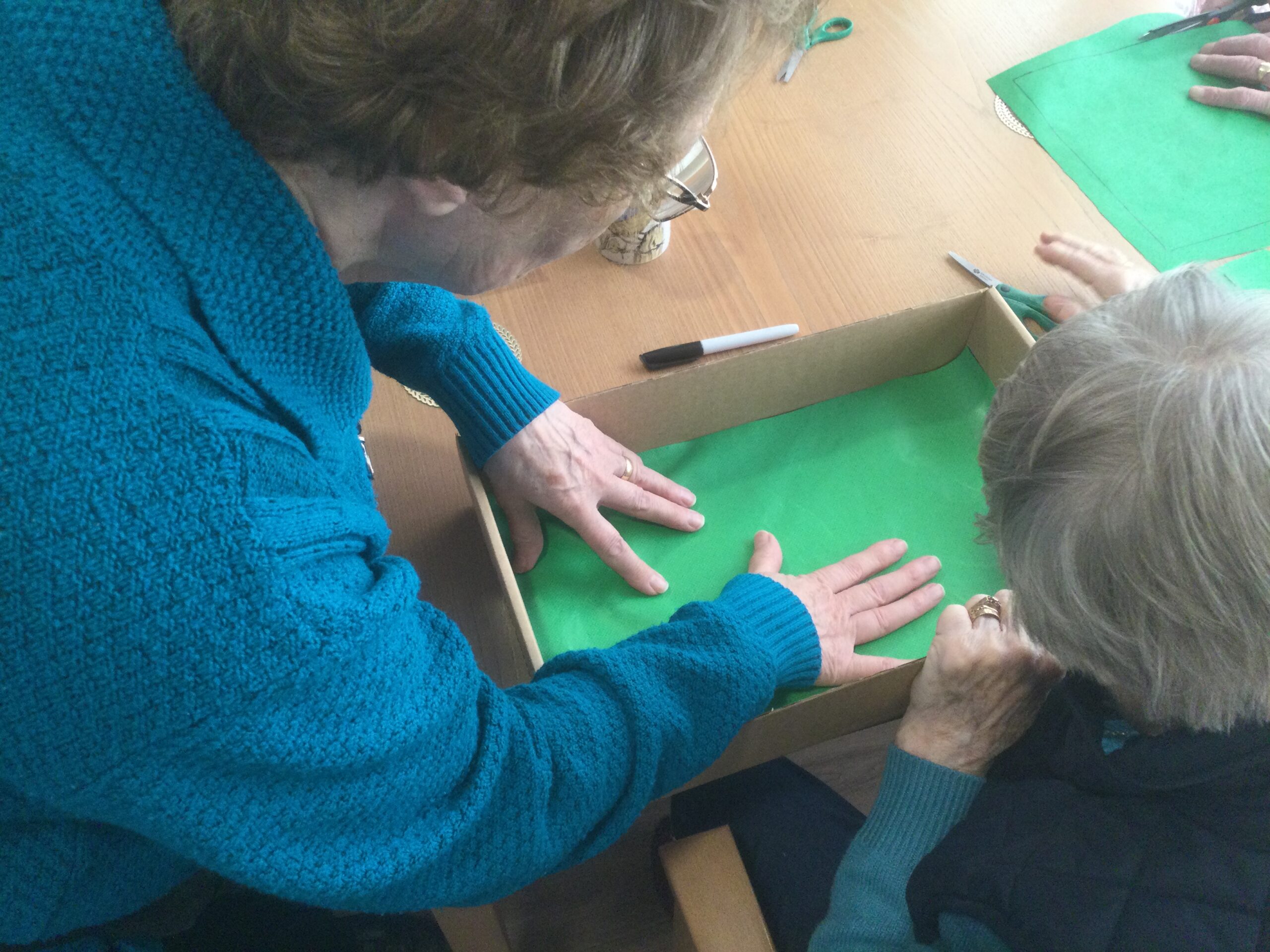 Overhead photo of two people lining a cardboard box with some green material