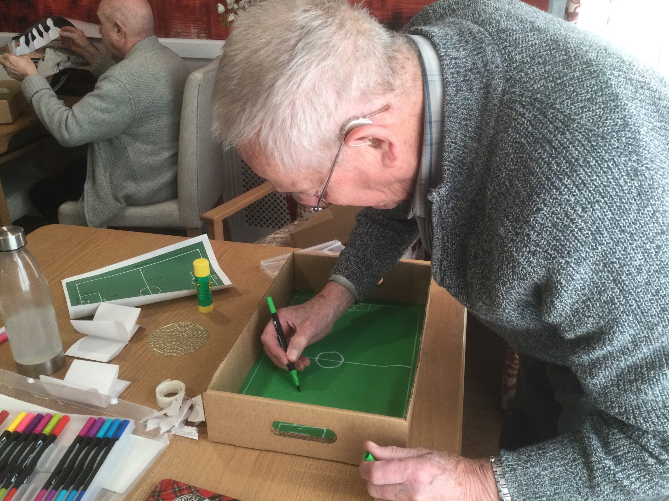 A gentleman leans over the cardboard box, marking out the lines