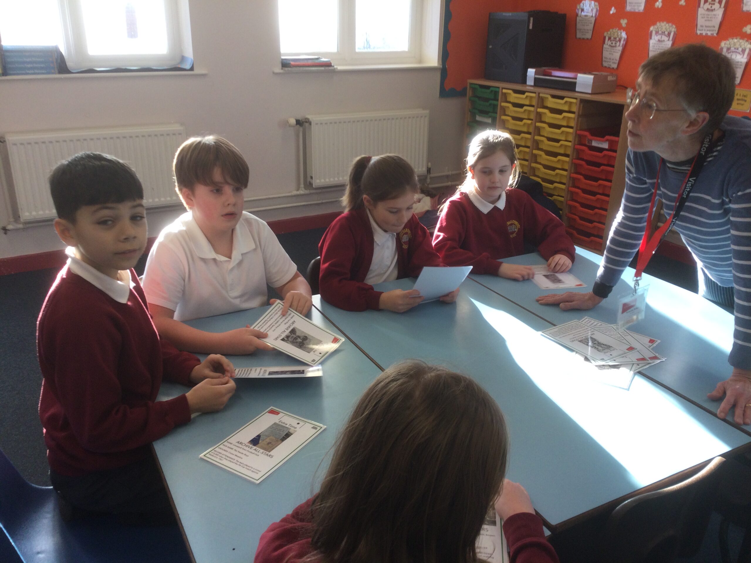 Children seated around a table looking at laminated cards with an adult standing by