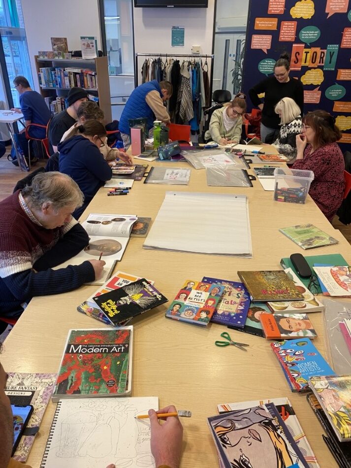 Learning disabled artists work together at a table covered in beautiful arts materials.