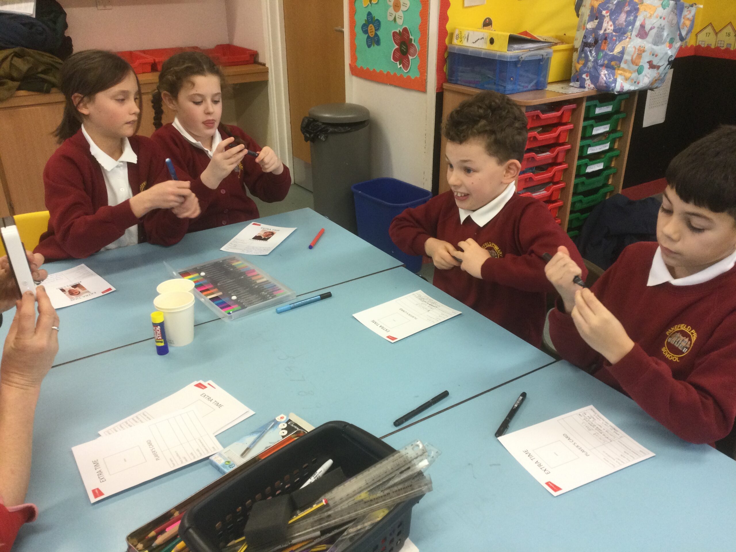 A group of school children seated at a table with pens, glue and paper in front of them