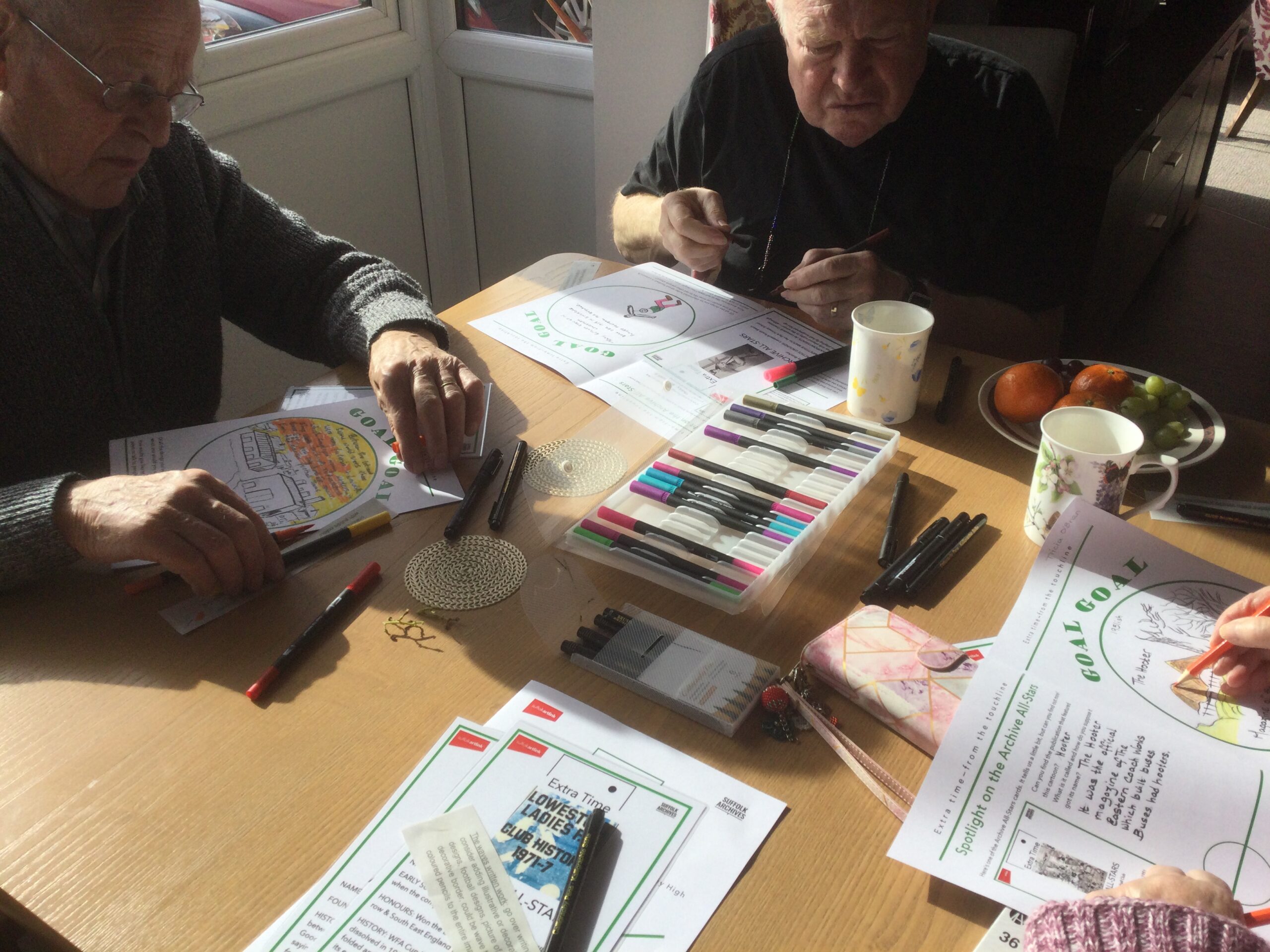 Adults seated around a table, with coloured pens and pencils scattered about, working on their illustrations