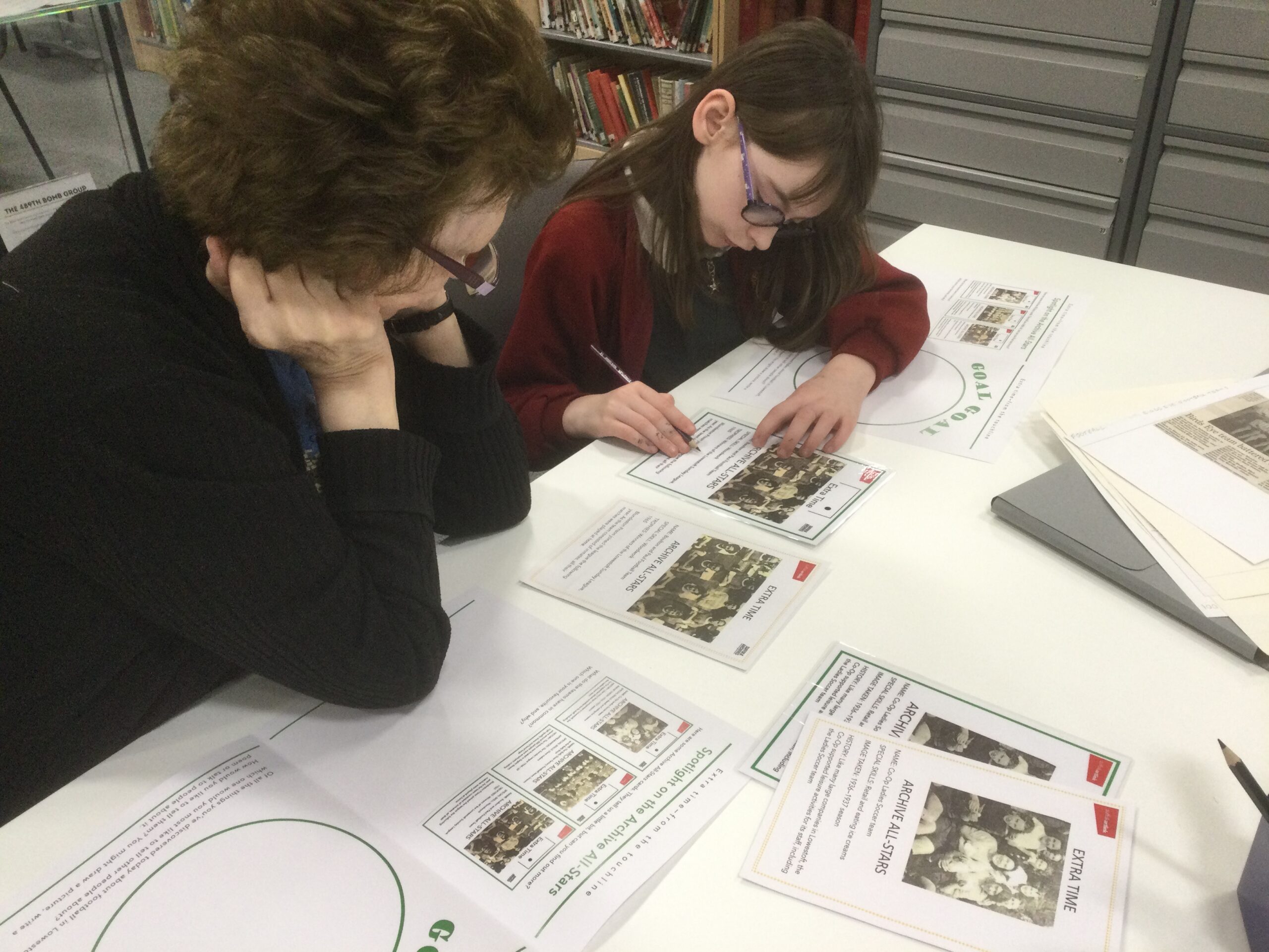 A school girl and adult, seated at a table, studying images