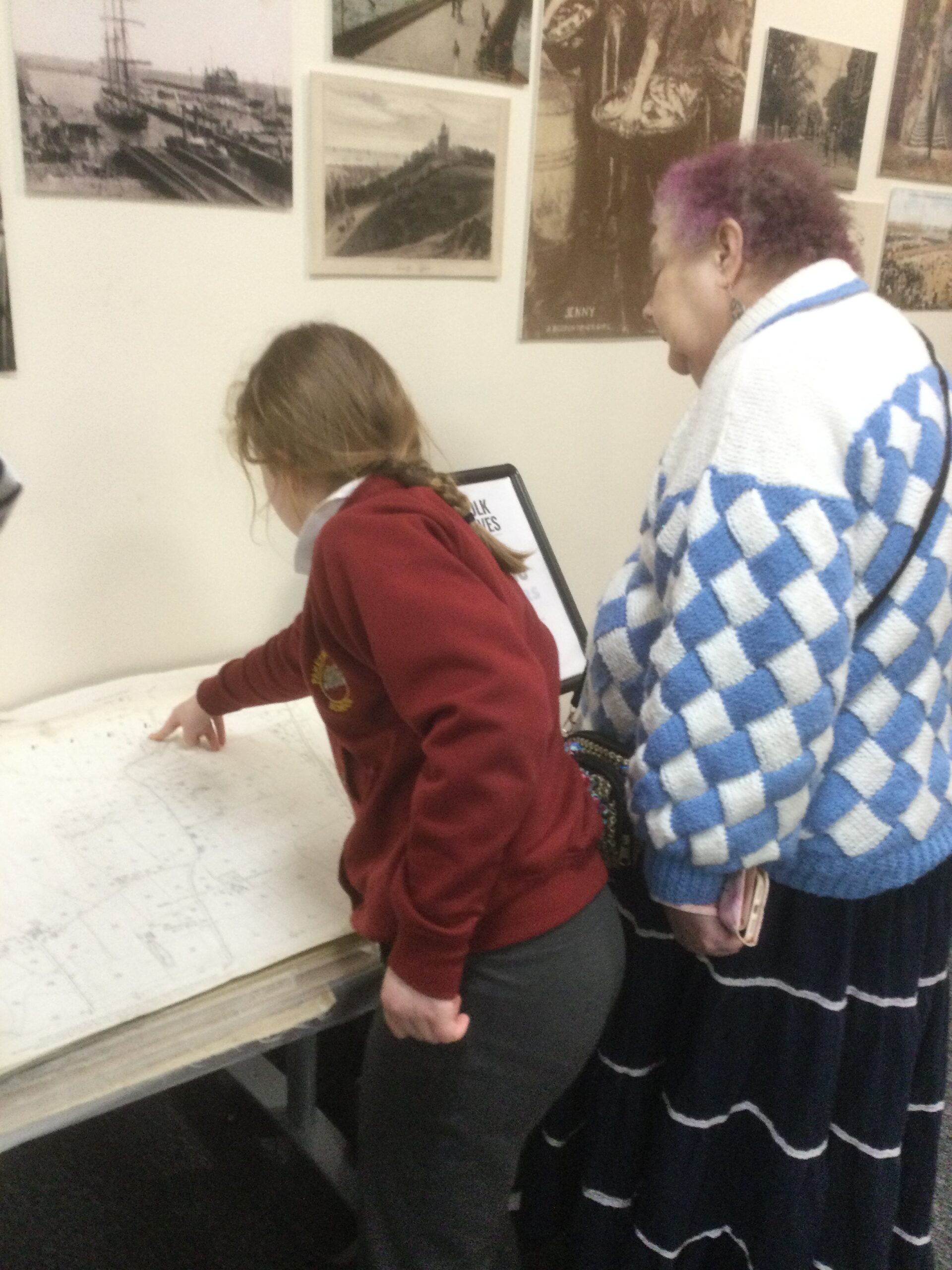 A woman and school girl standing side by side looking at an old map of Lowestoft