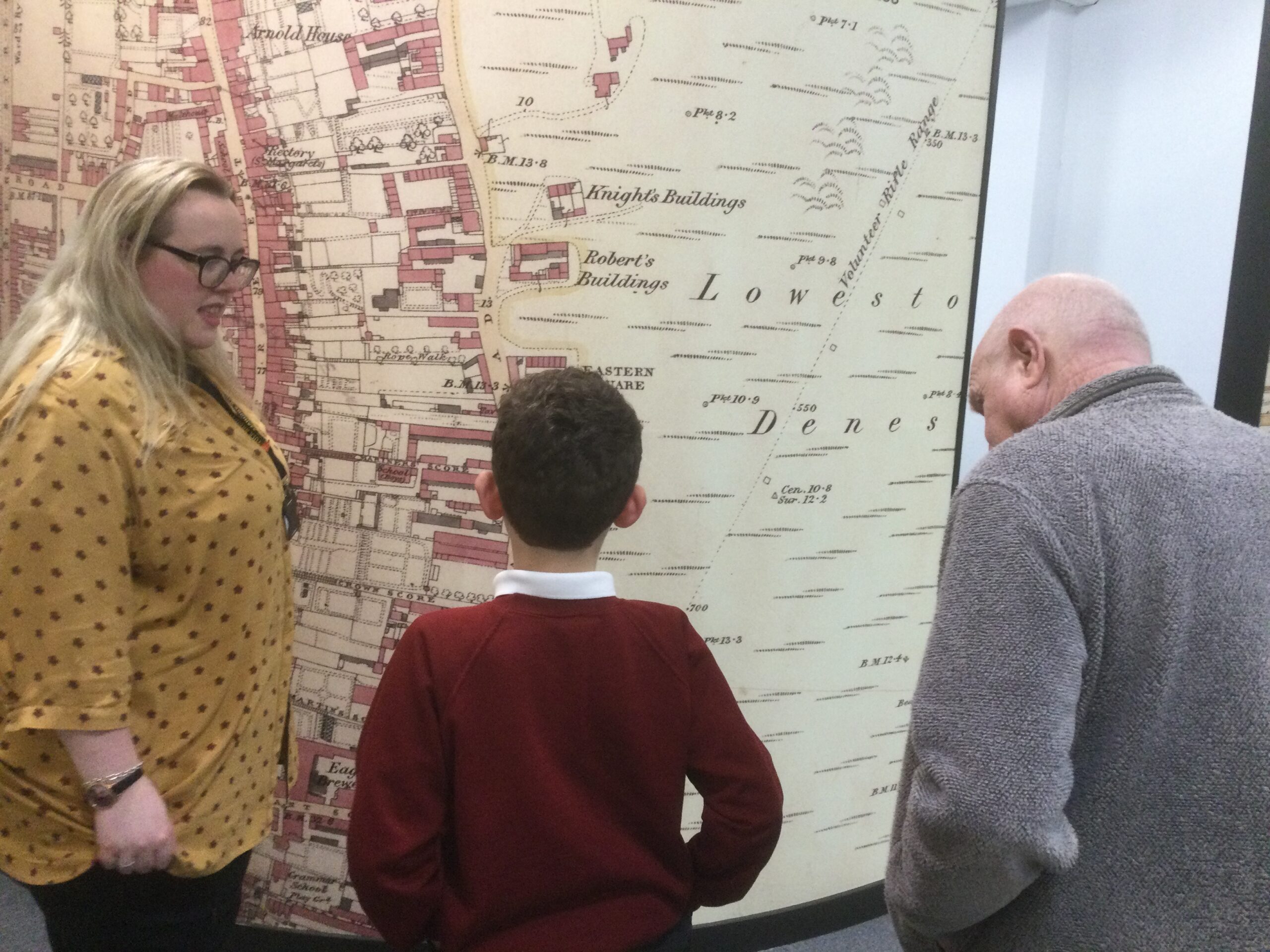 A gentleman and school boy looking at the wall map together with member of the Archive staff