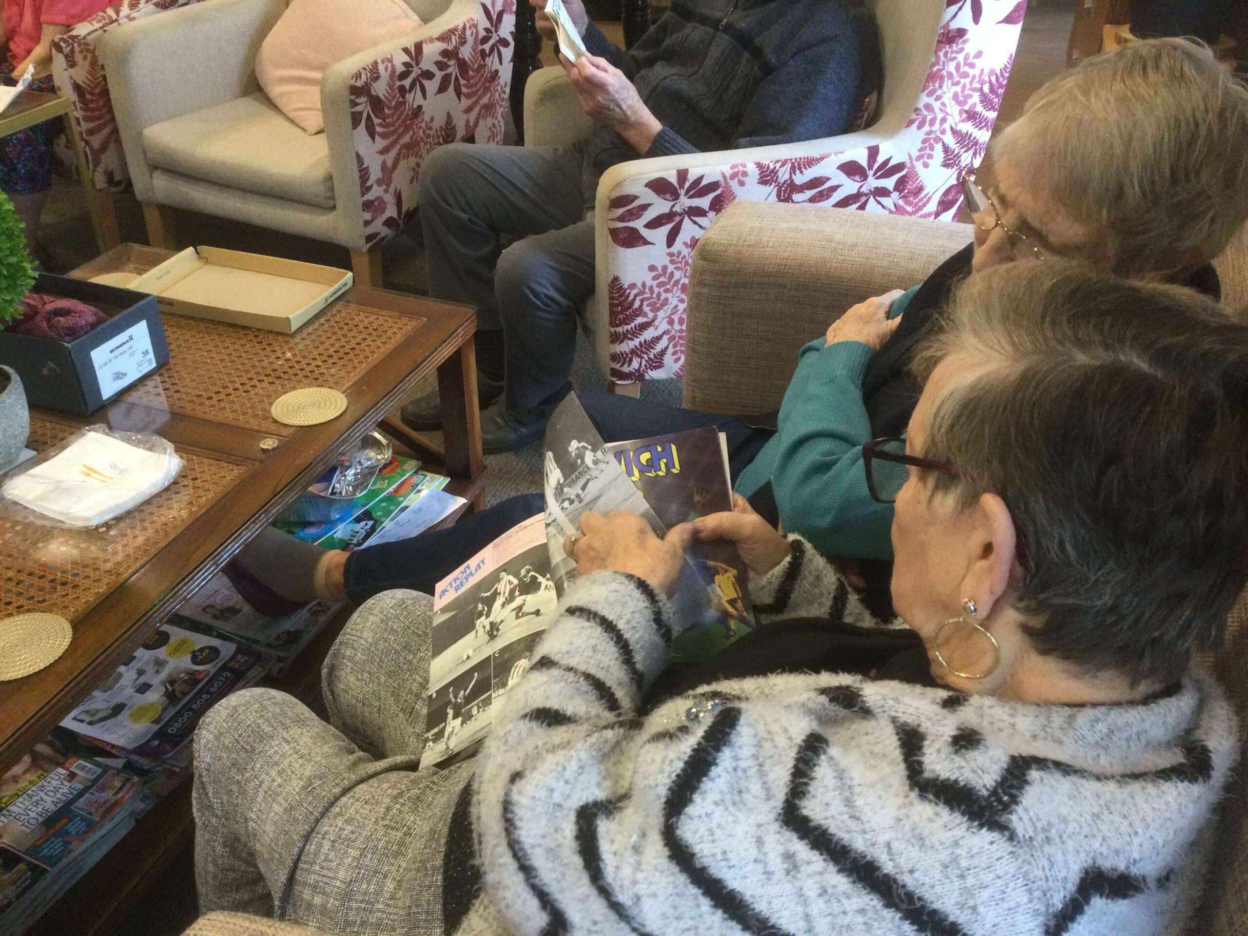 Two women seated on a sofa looking through a football programme