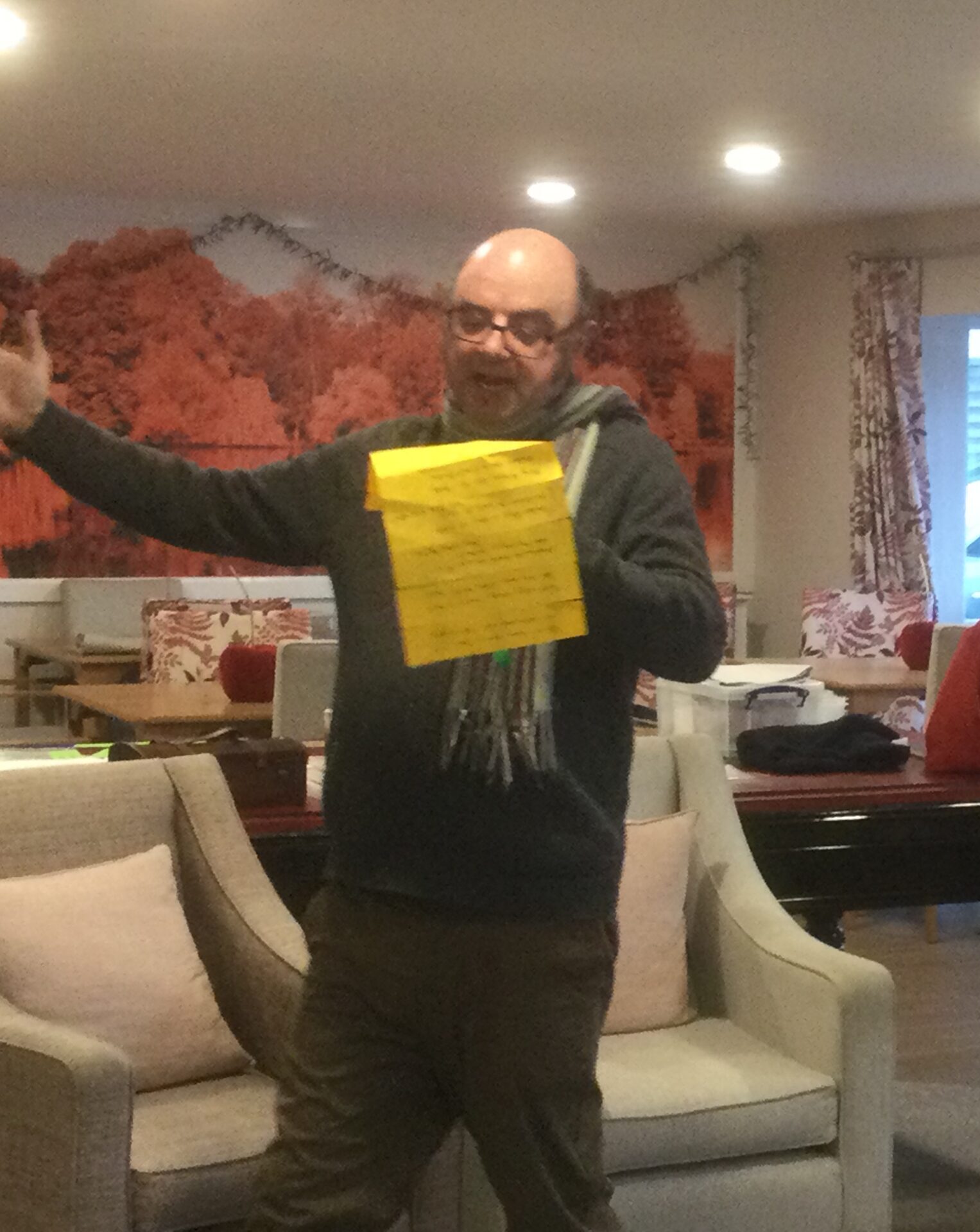 A man stands, arm outstretched, reading from a yellow piece of paper