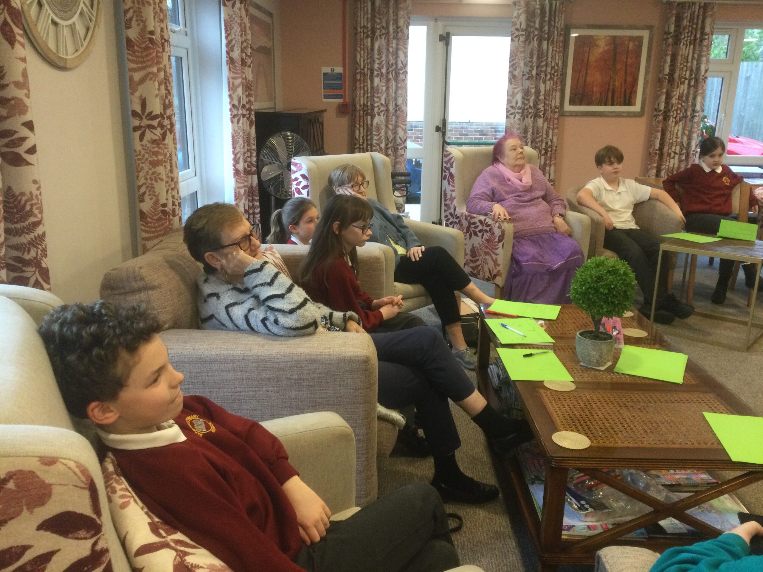 A mixed group of adults and children seated in easy chairs around a low table