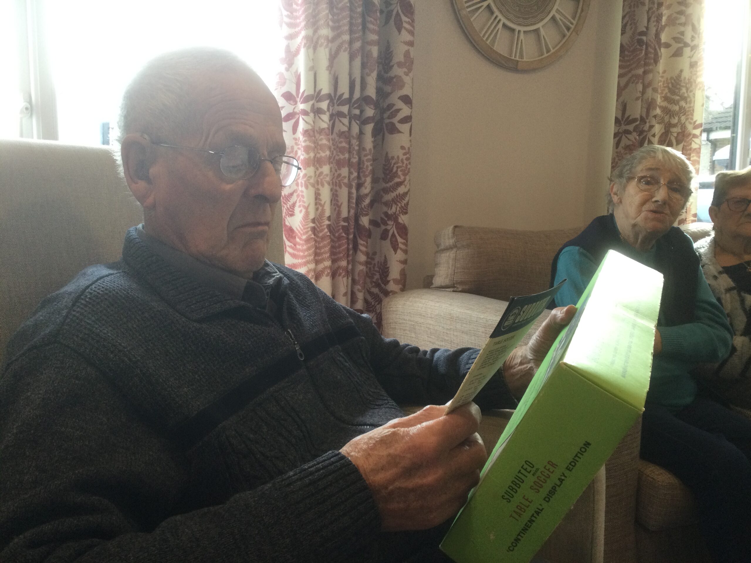 A gentleman holds the lid of a Subbuteo table soccer game as he reads the instructions