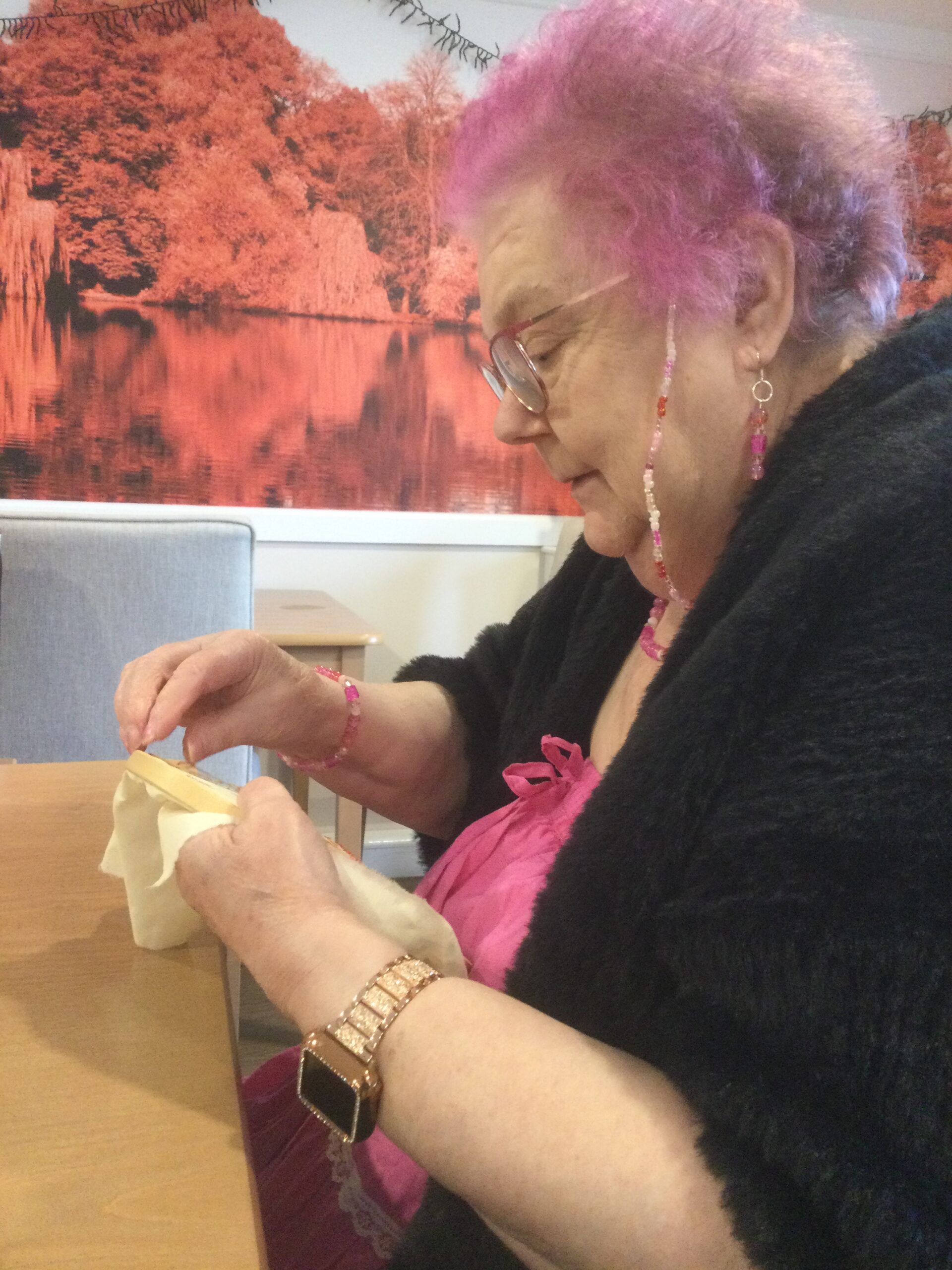A woman with pink hair and wearing a black shawl is stitching some embroidery