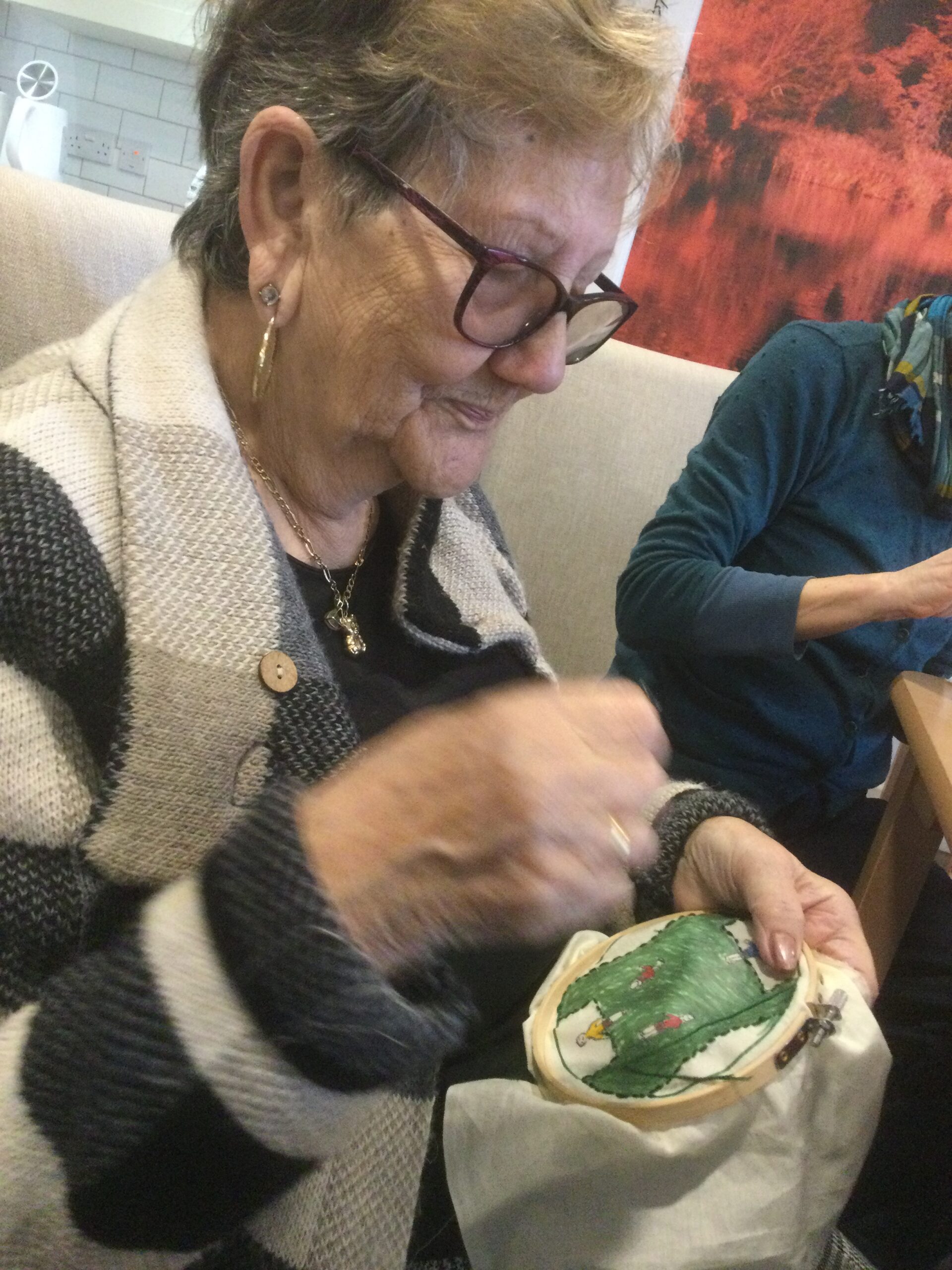 A woman wearing a striped jacket stitching a green piece of embroidery