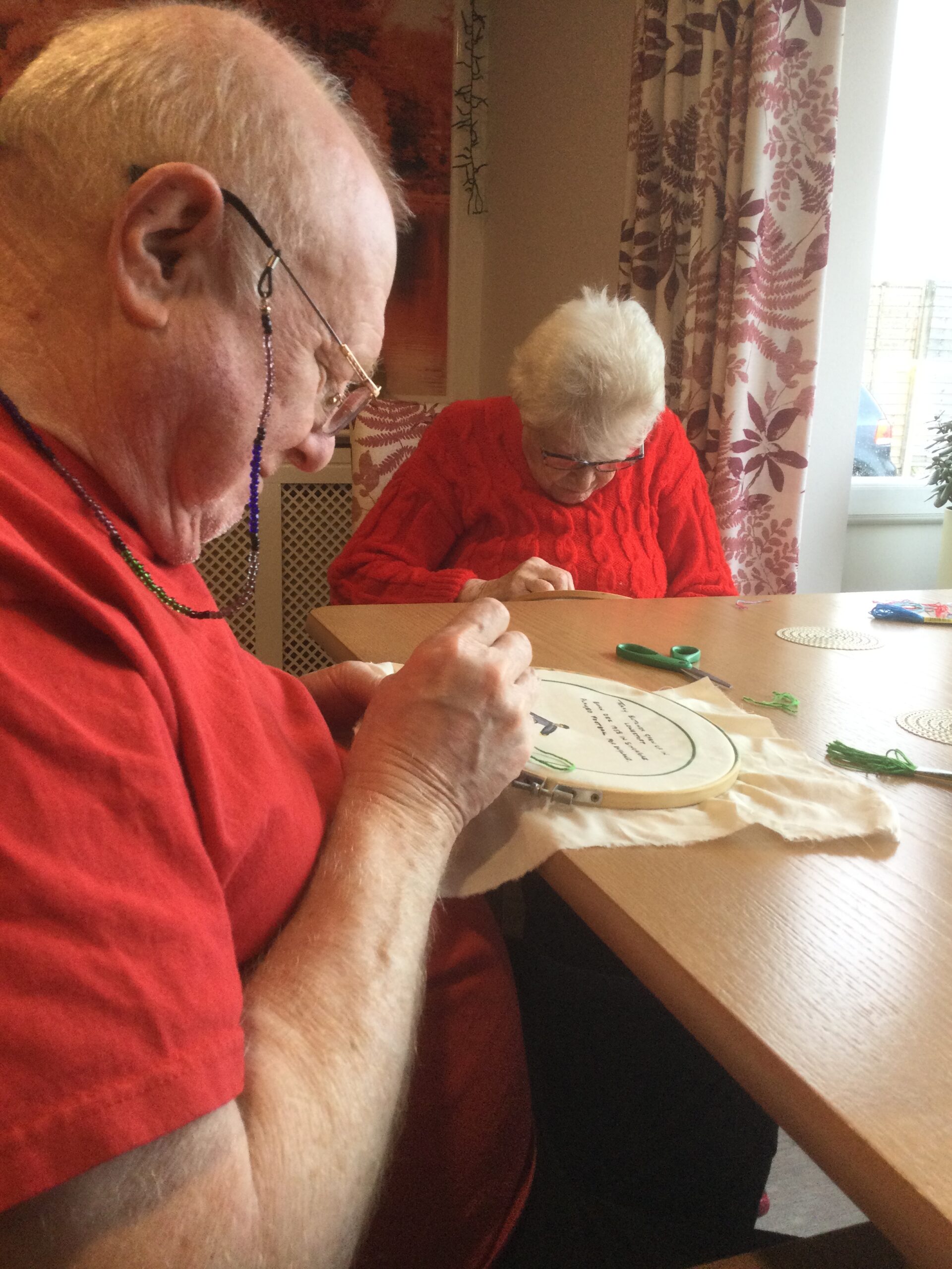 Two adults, each wearing red tops, sit concentrated on the work they're doing