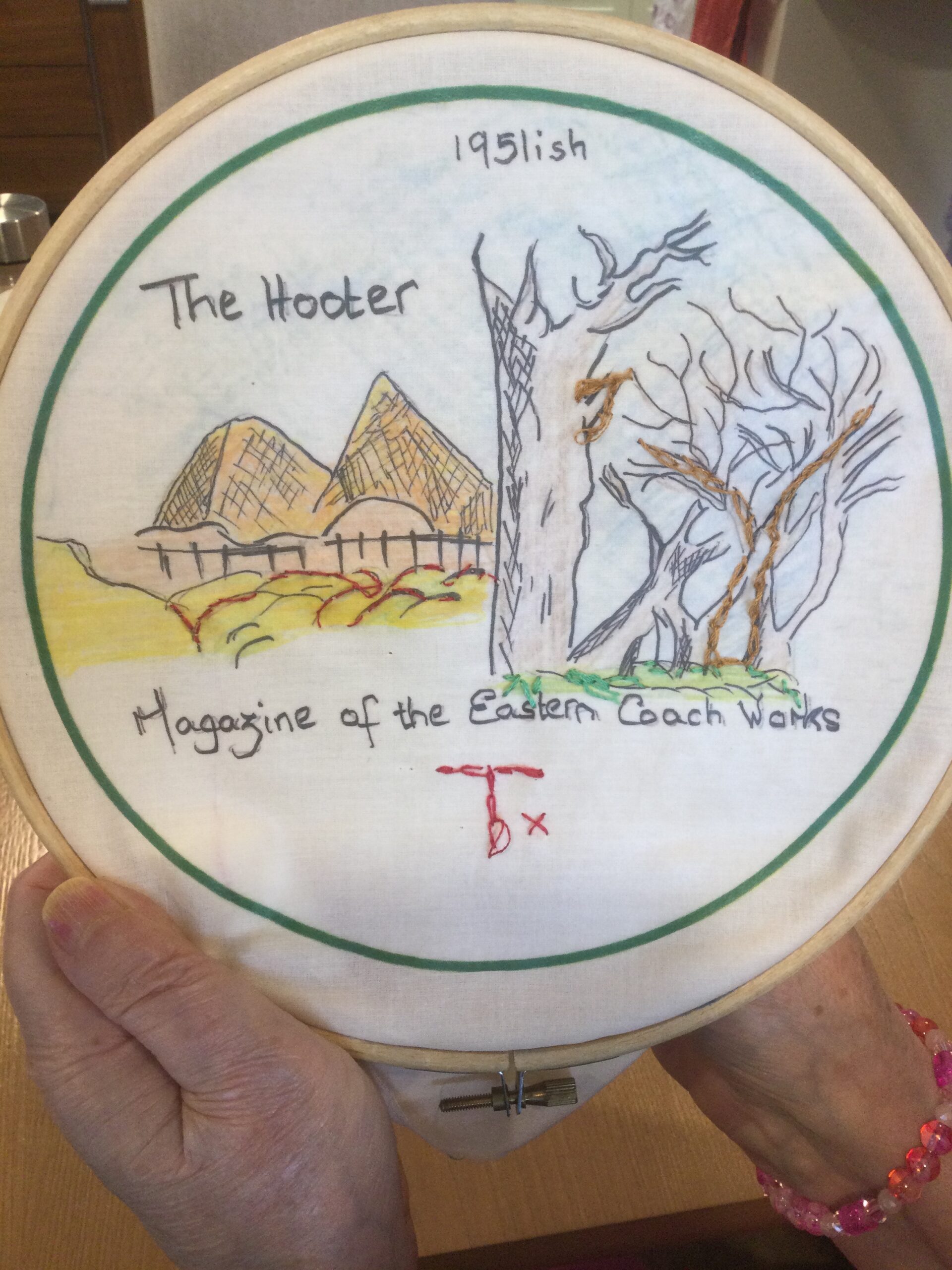 A piece of embroidery in a wooden hoop, showing the cover of the Hooter magazine
