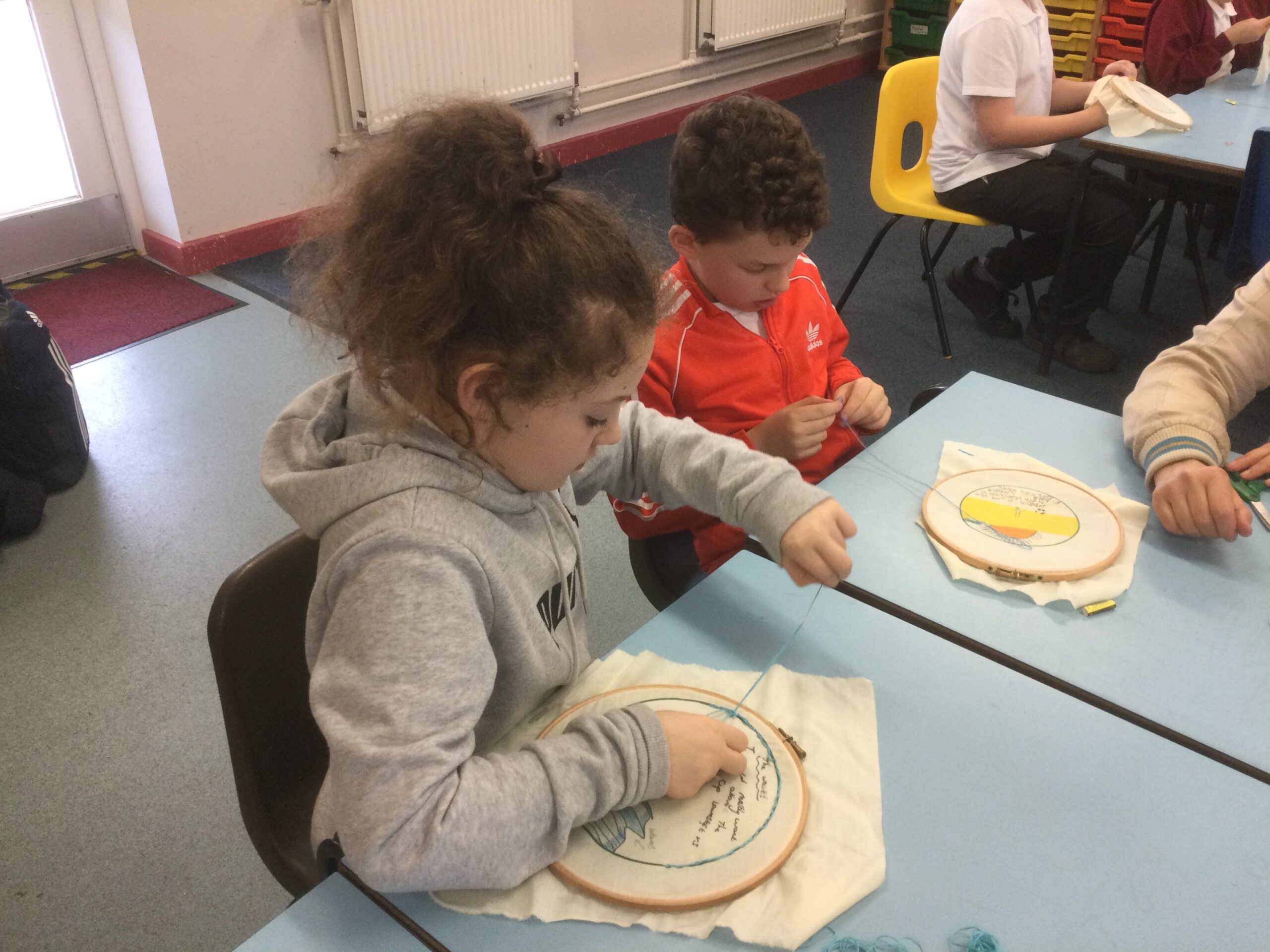 School children seated at tables doing their embroidery