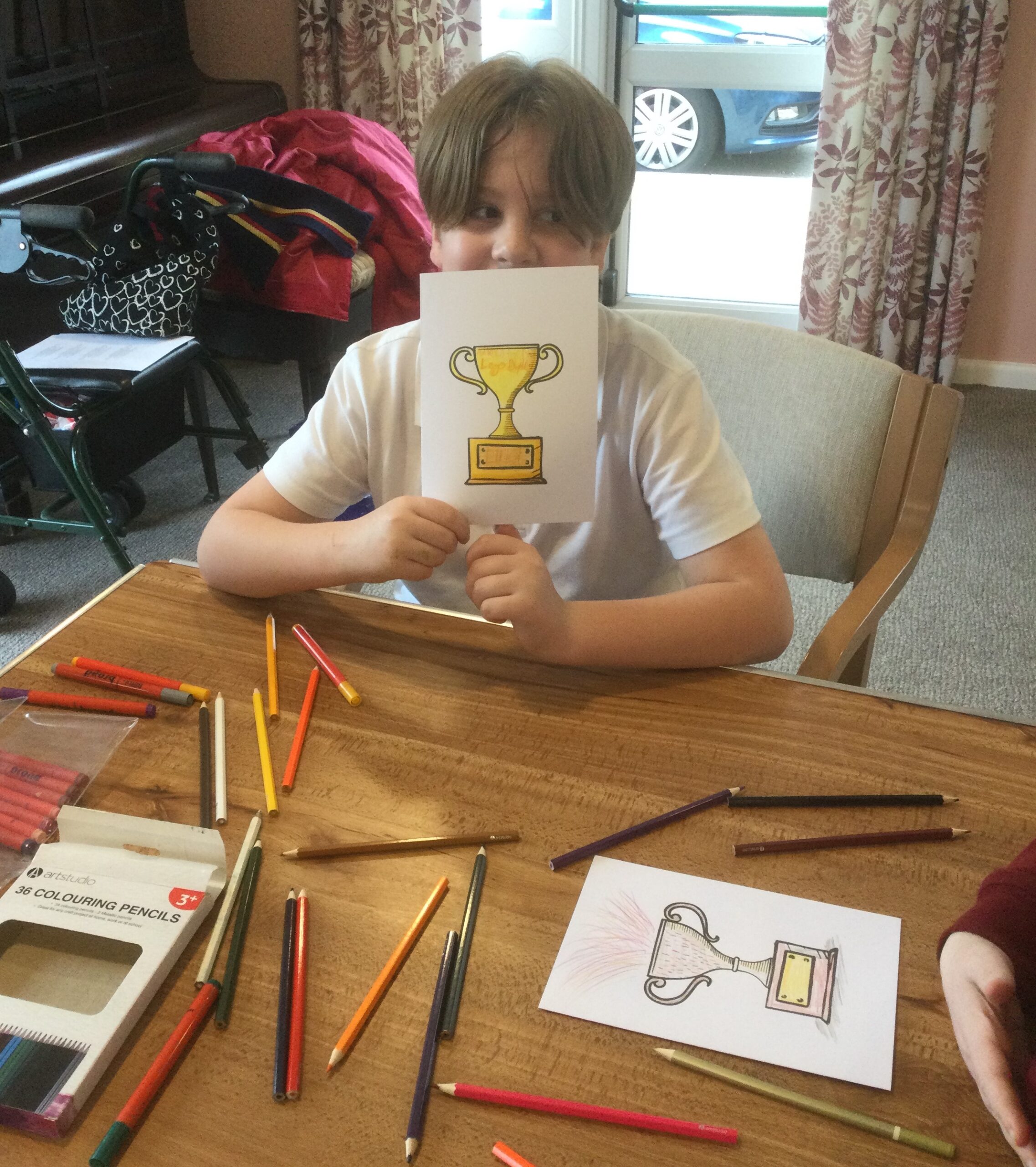 A school boy holds up a card on which he's coloured a bright yellow trophy