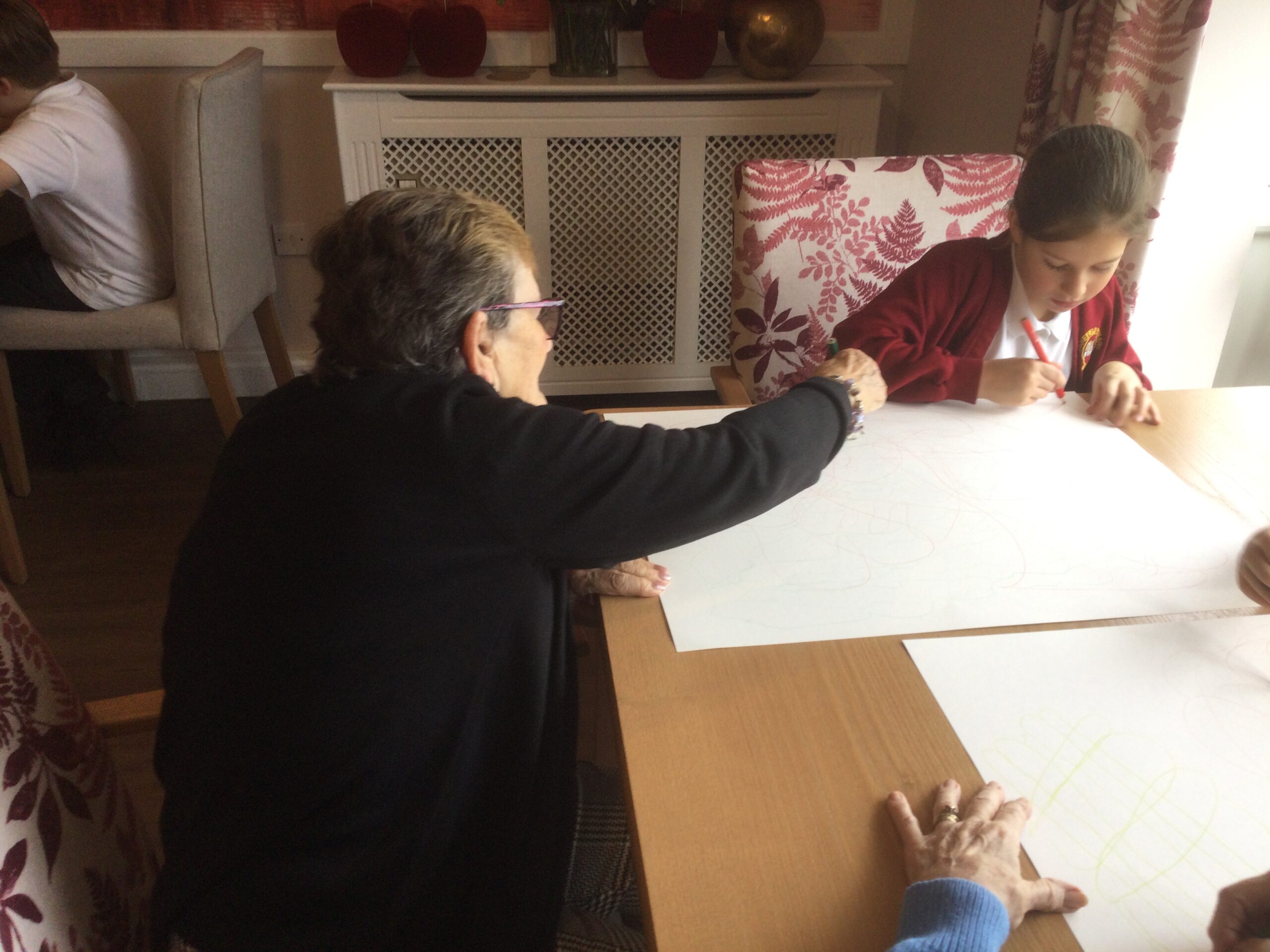 Large sheets of paper on a table top with adults and a school child drawing on them