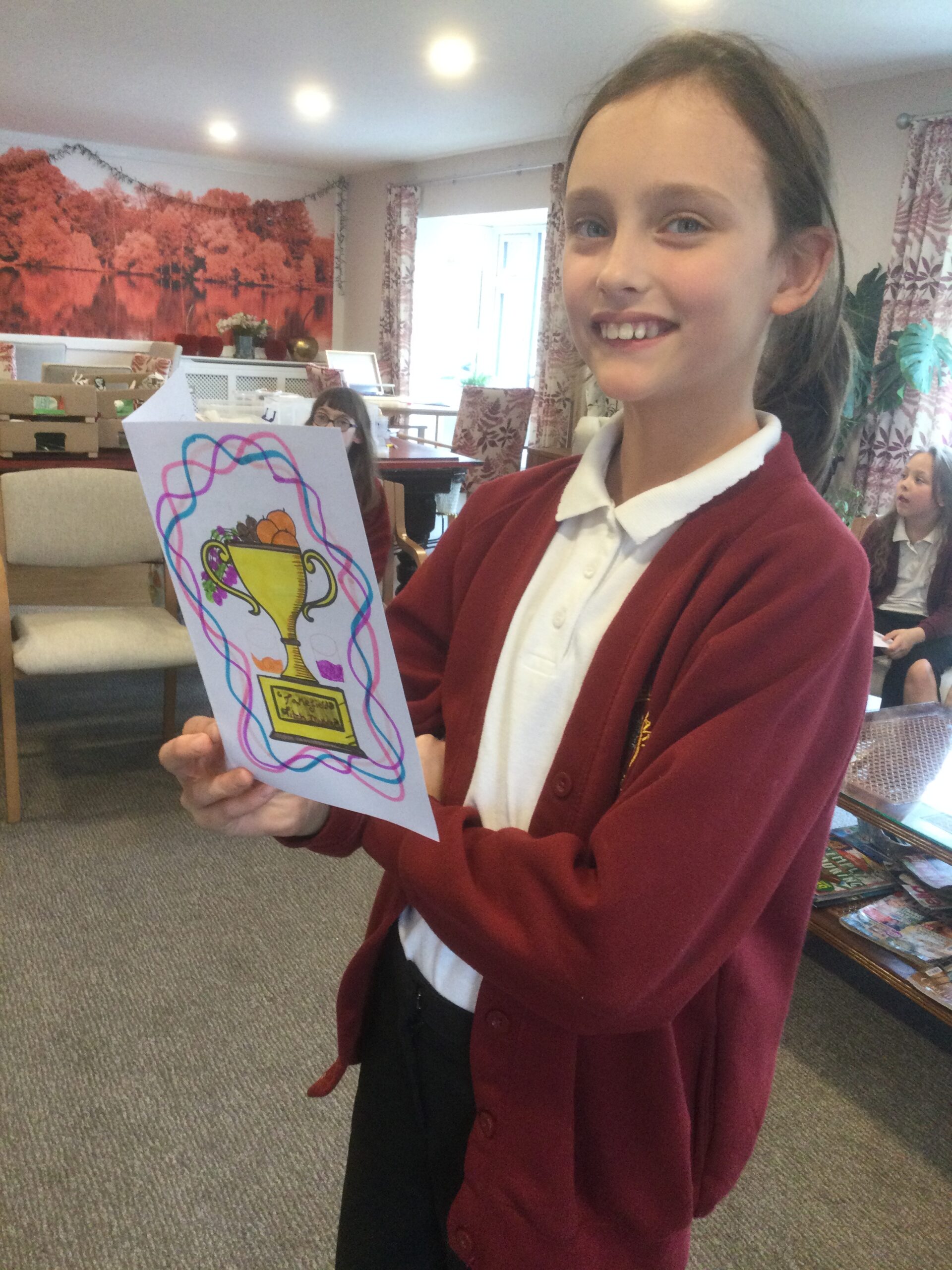 A child beams at the camera, and is holding a card with a decorated trophy on the front