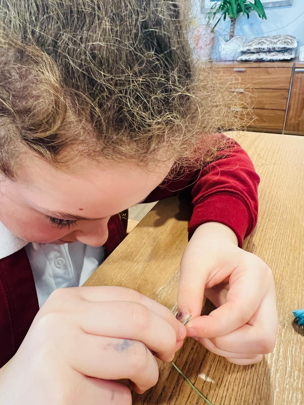 A child peers intently at a needle as she attempts to thread it