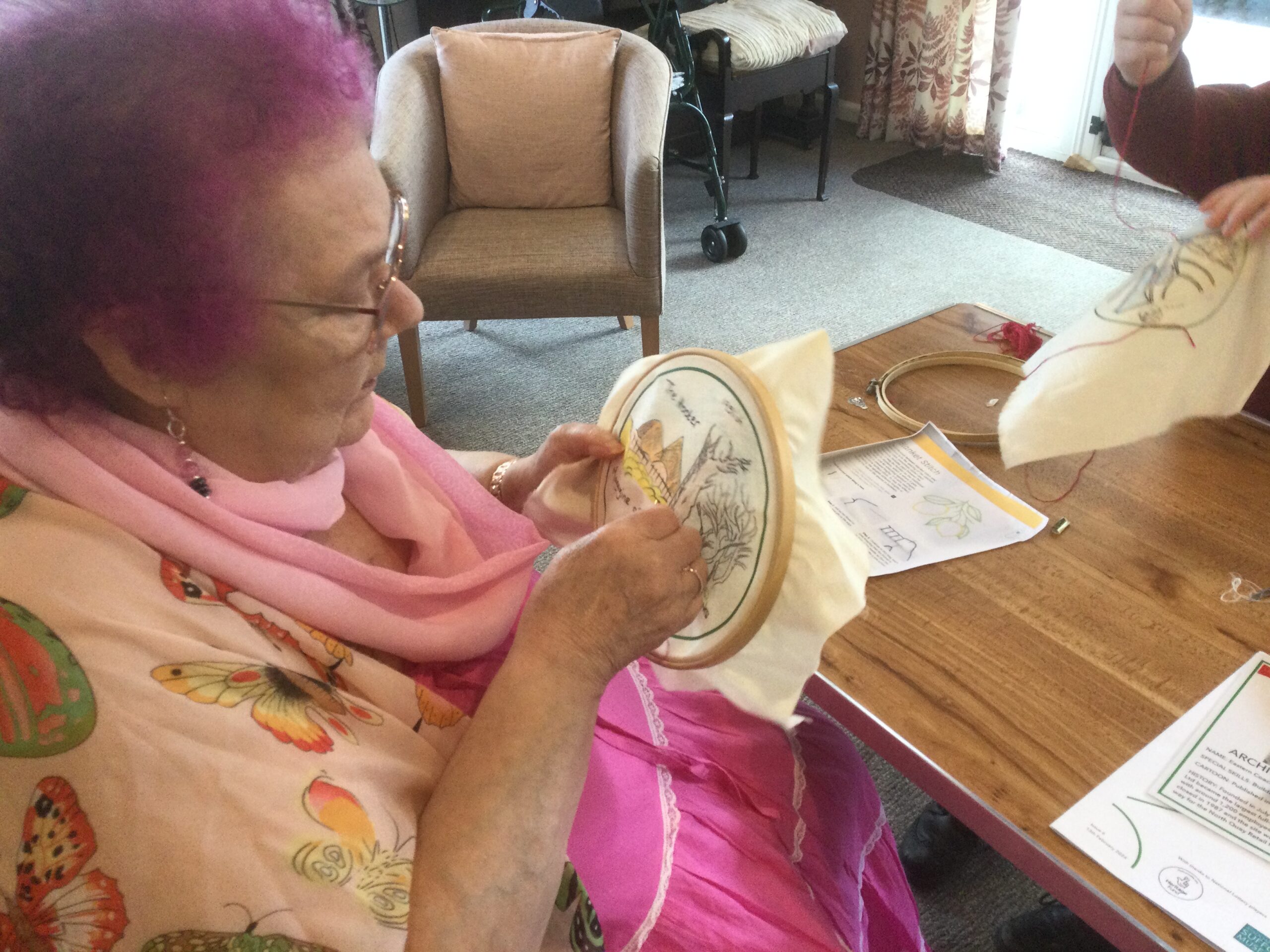 A woman dressed predominantly in pink embroiders a printed picture