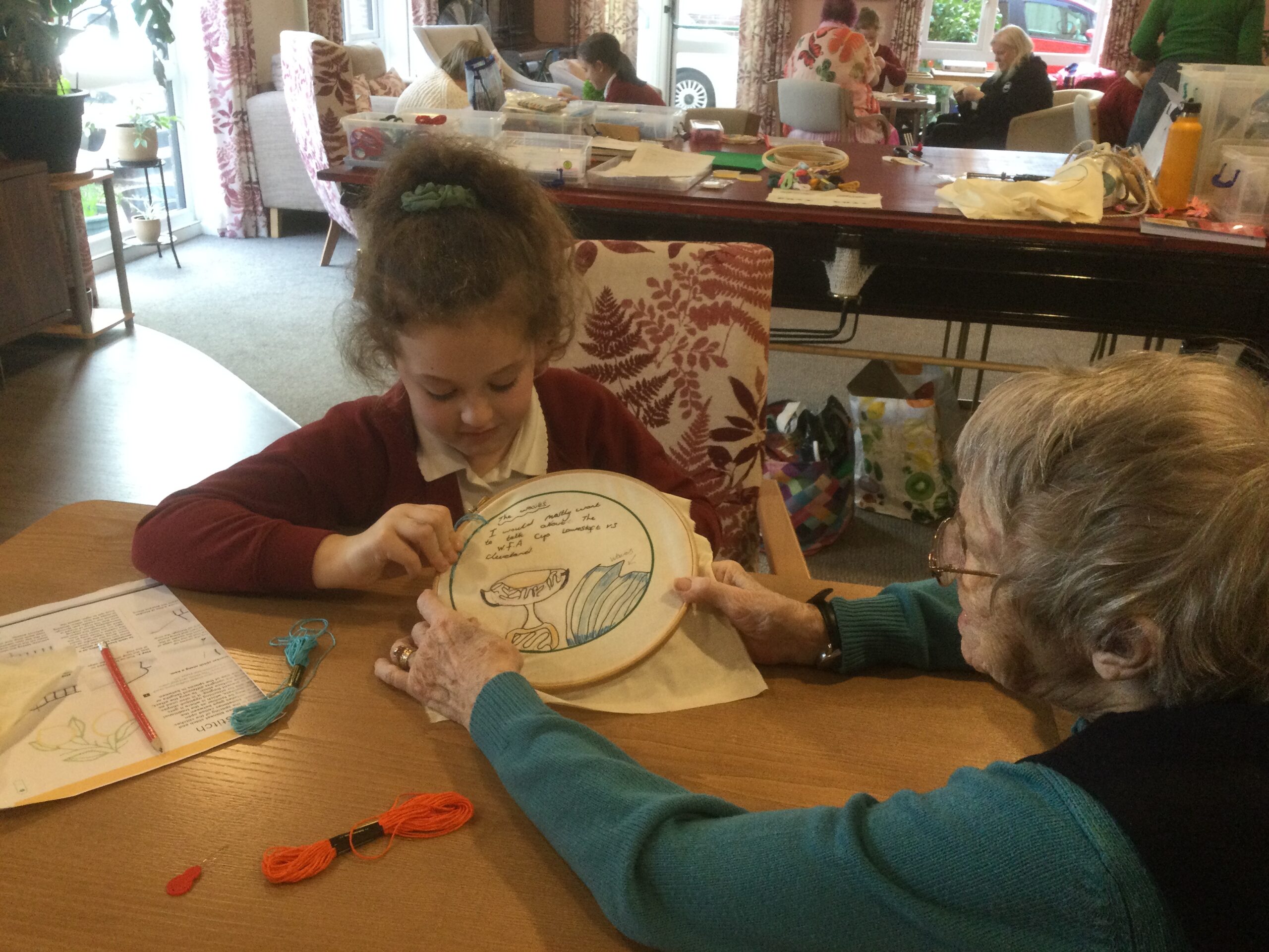 A woman holds the embroidery hoop steady whilst the child stitches onto the fabric