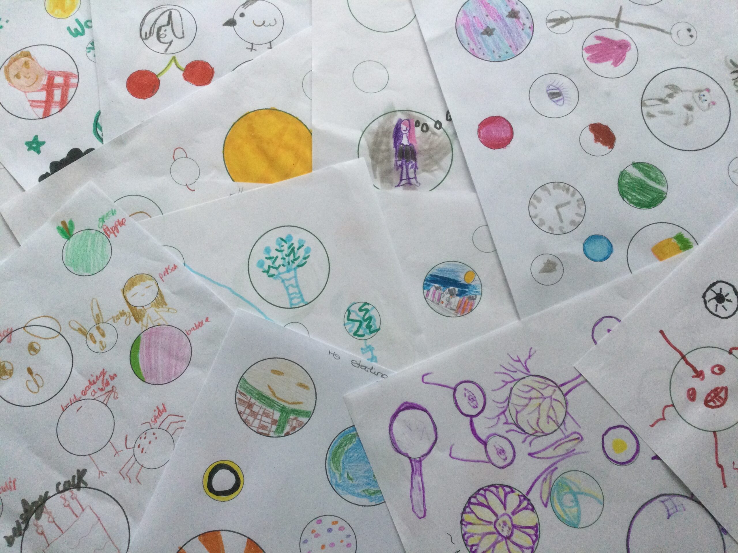 Overlaid sheets of paper printed with different sized circles, many of which have been decorated and redrawn as objects such as spectacles, cherries and clock faces