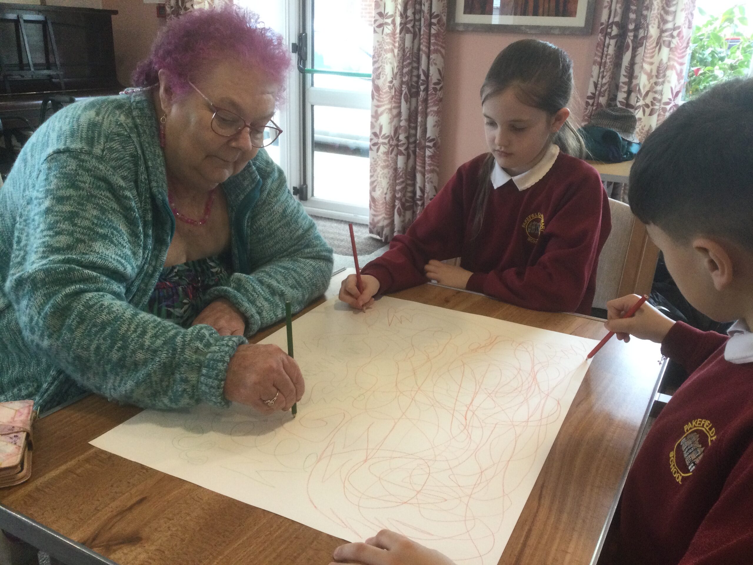 Two school children and an adult drawing random lines on a large piece of paper