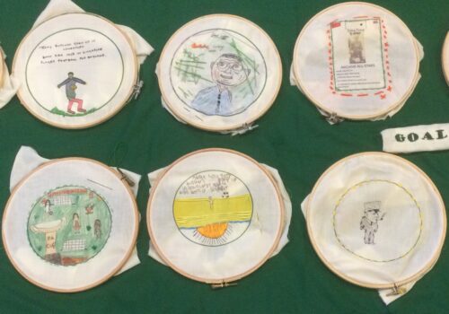 A row of embroidery hoops each with a different stitched images laid out on a green background