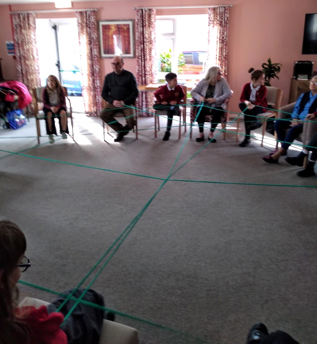 A circle of adults and children with lengths of yarn stretched across the room, connecting them all