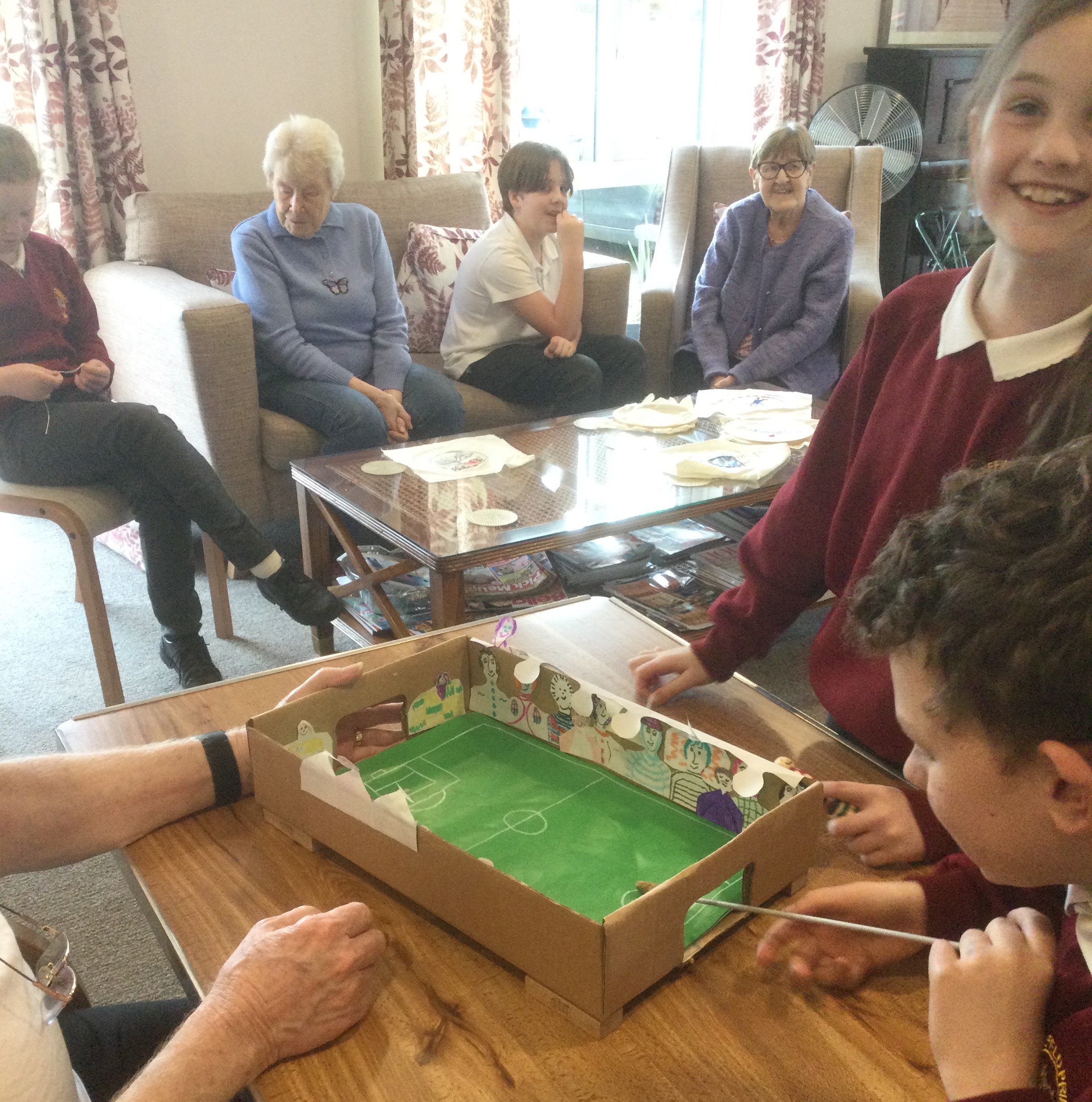 In the background a group of mixed adults and children chatting and in foreground a table top football game with children playing