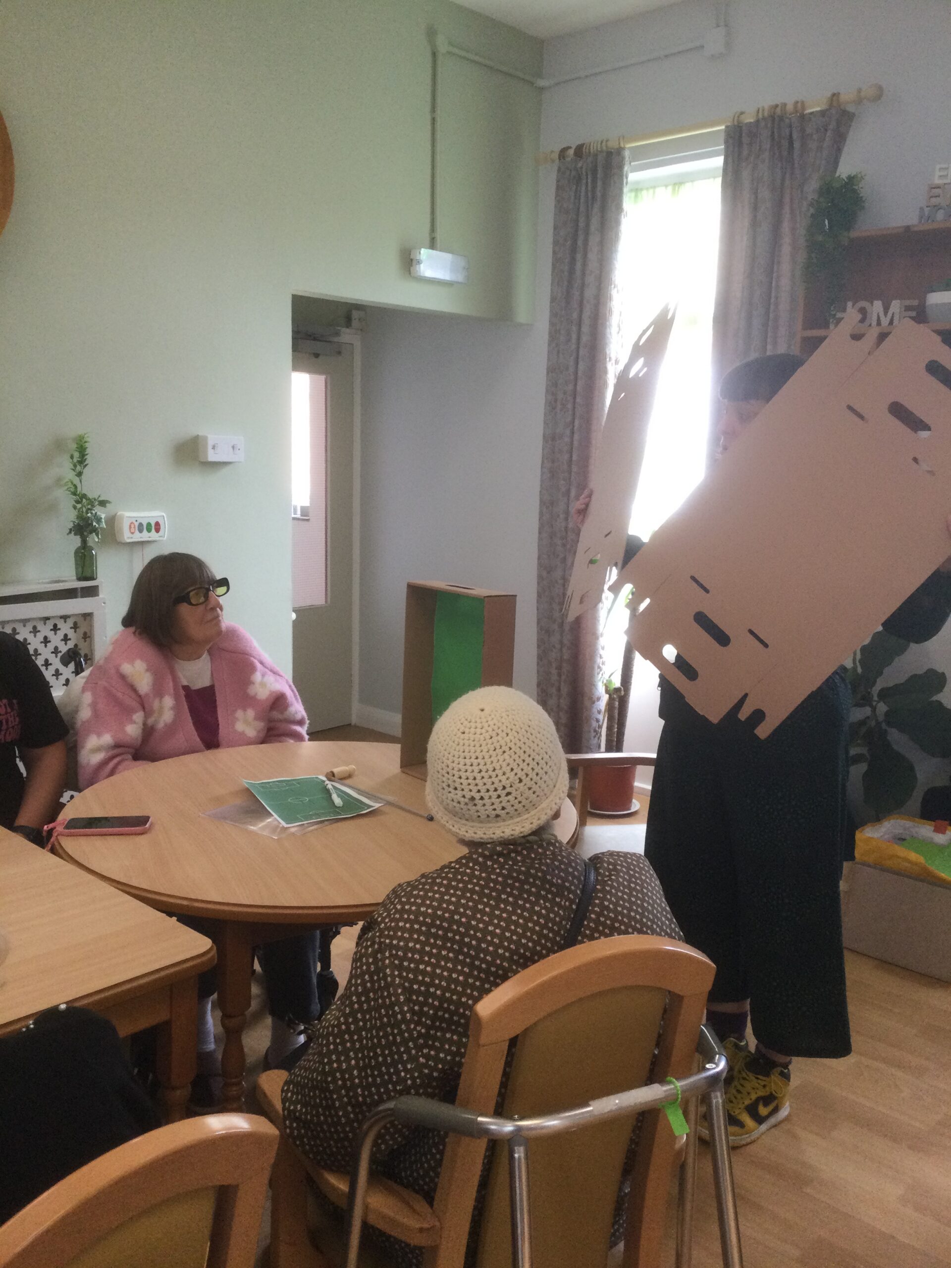 A person holding up a flat piece of cardboard showing it to people seated at a table