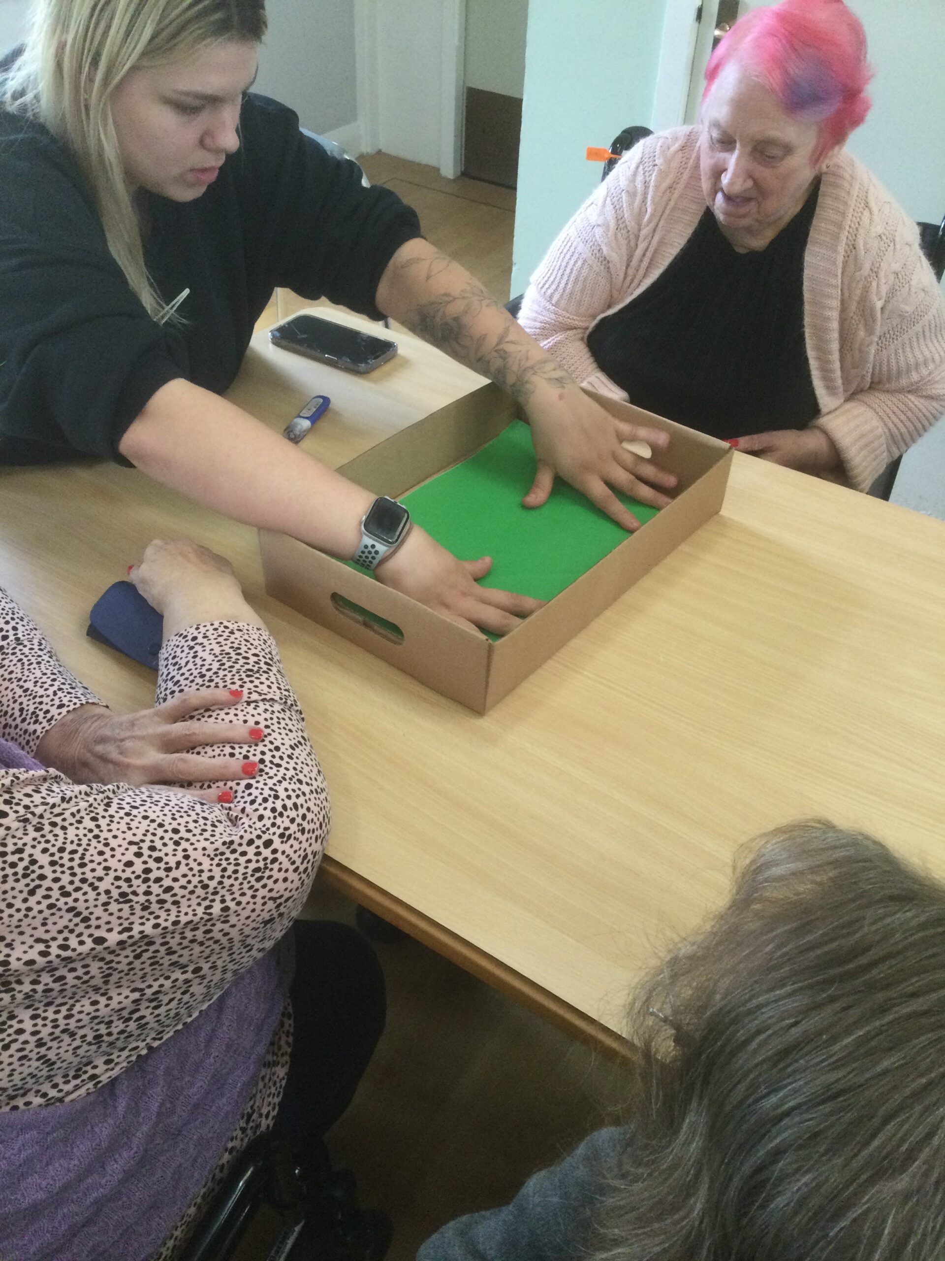 A woman dressed in a black jersey spreads a piece of green material inside the cardboard box