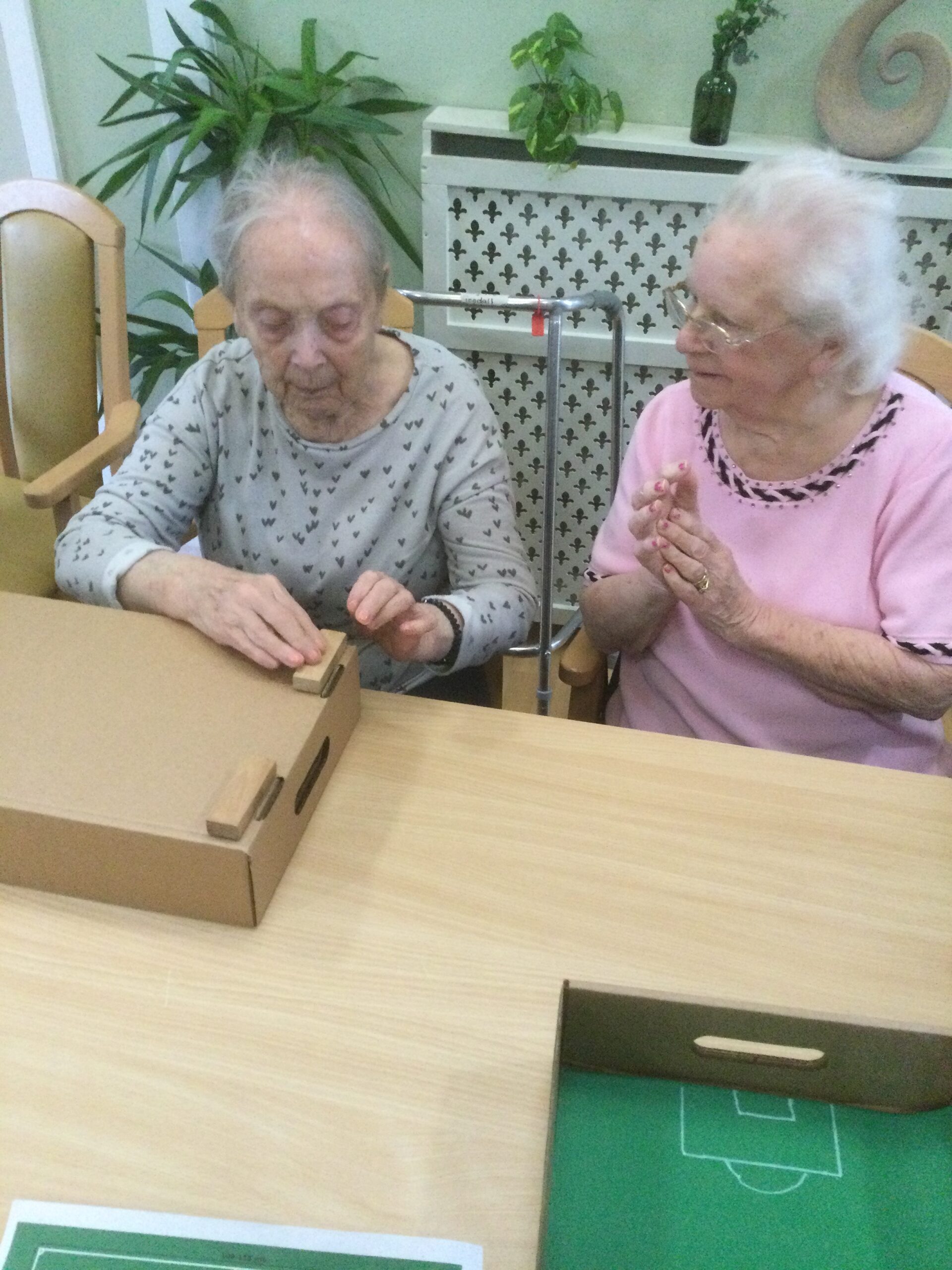 Two elderly women sticking wooden blocks to the bottom of a cardboard box