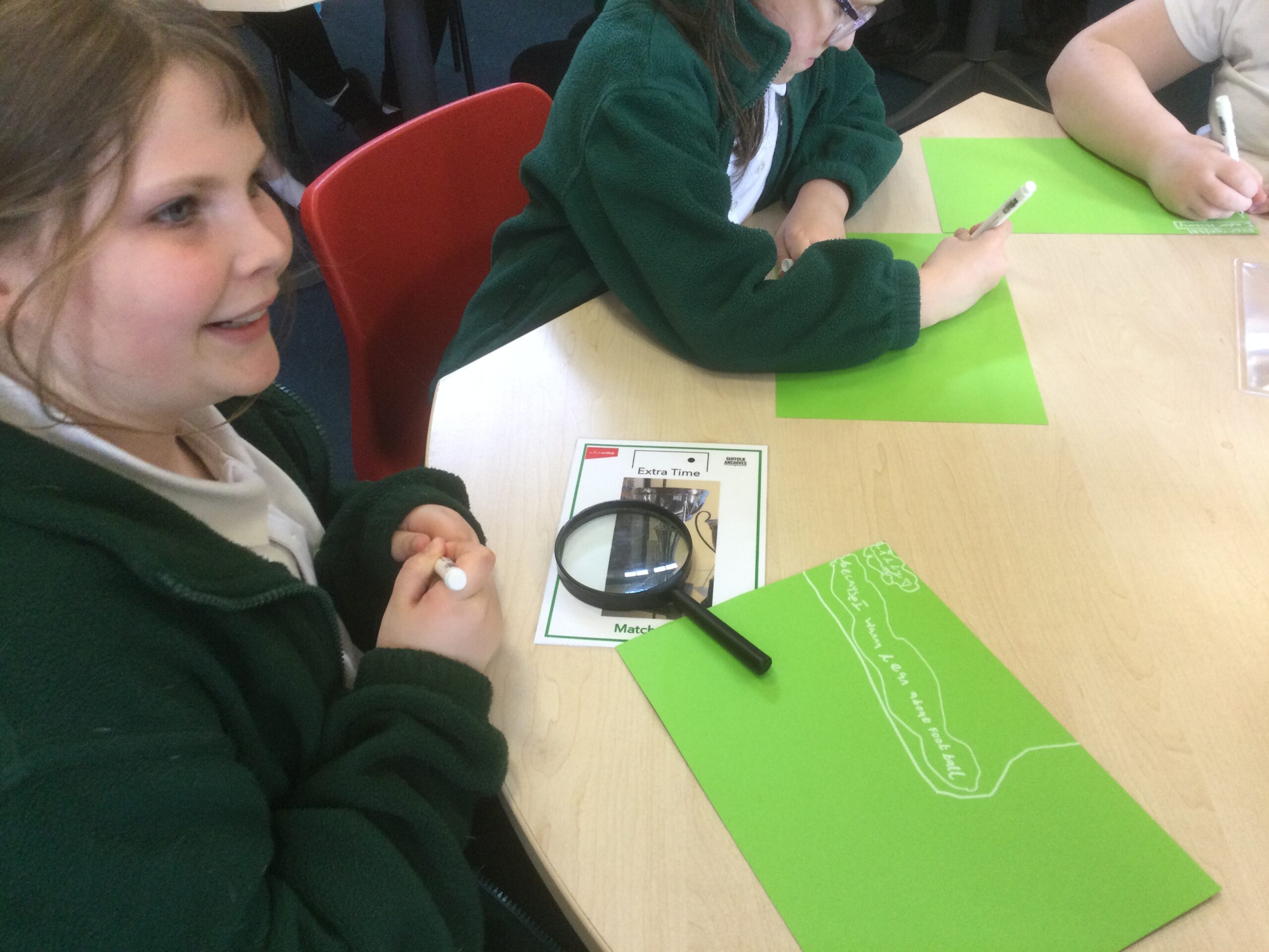 School children writing on green paper with white pens