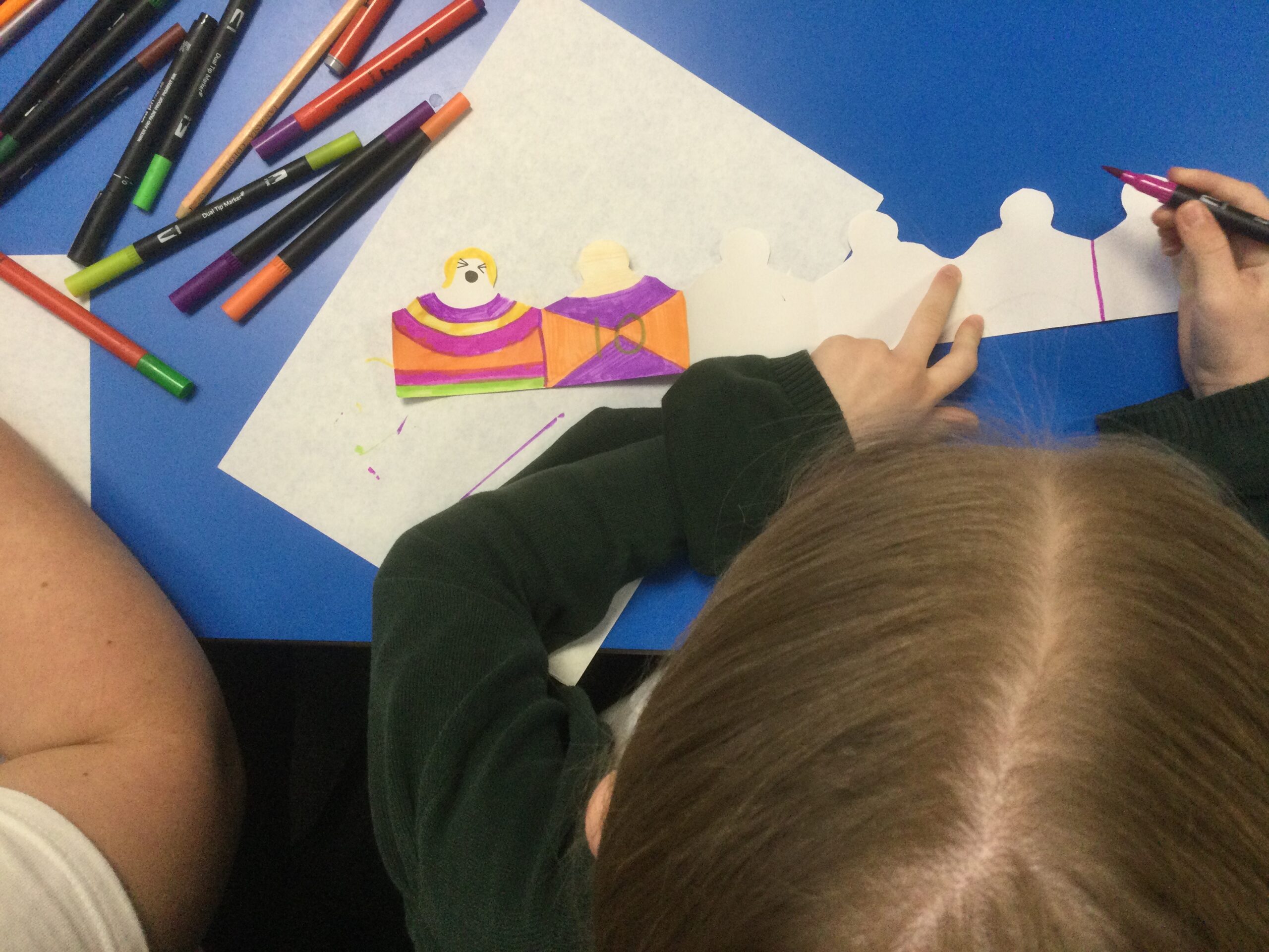 Overhead of child drawing paper people and colouring them in orange and purple