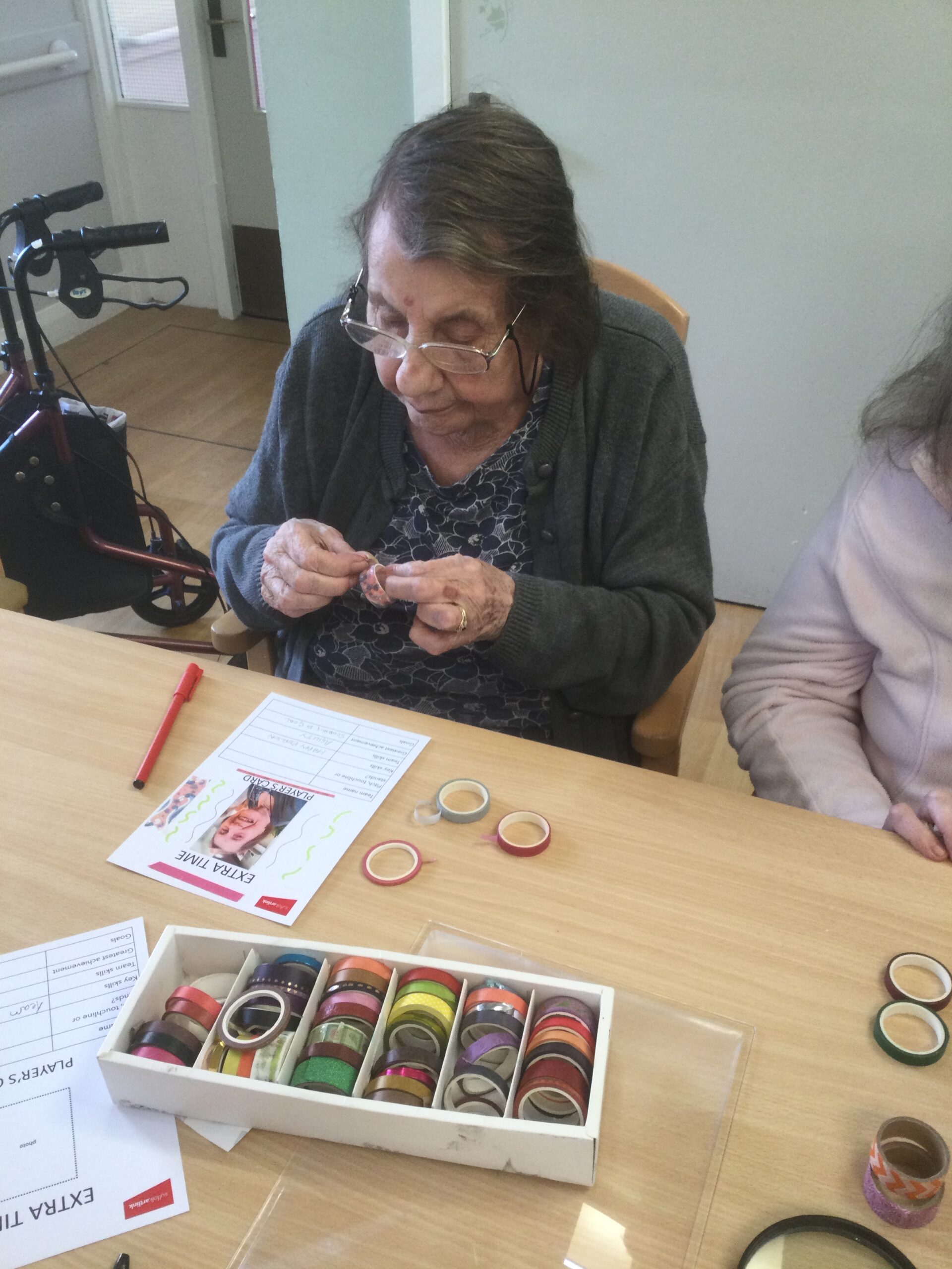 A woman unrolls a piece of coloured tape with which to decorate a card she is making.