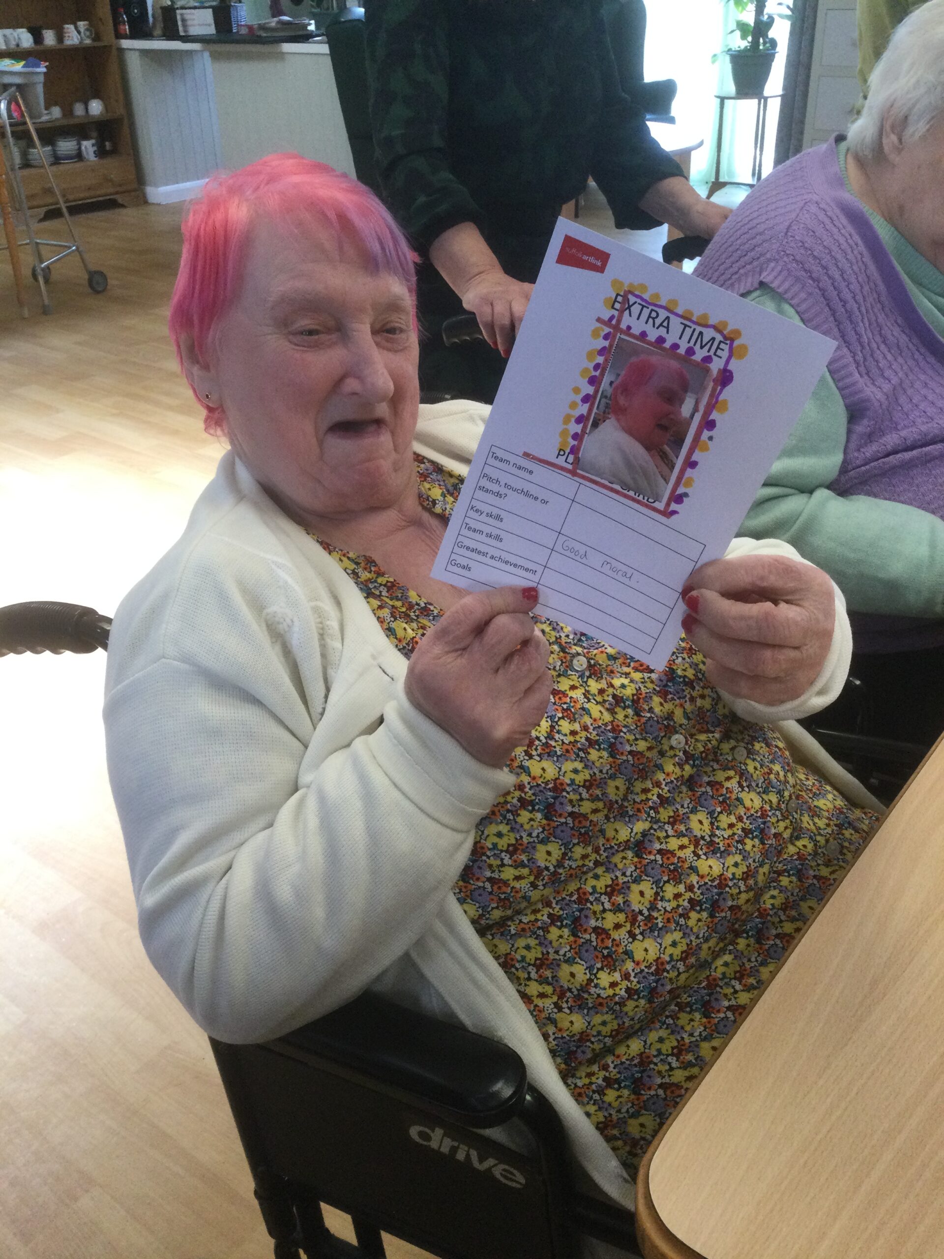 A woman holds up a card featuring a photograph of herself decorated with yellow and pink markings