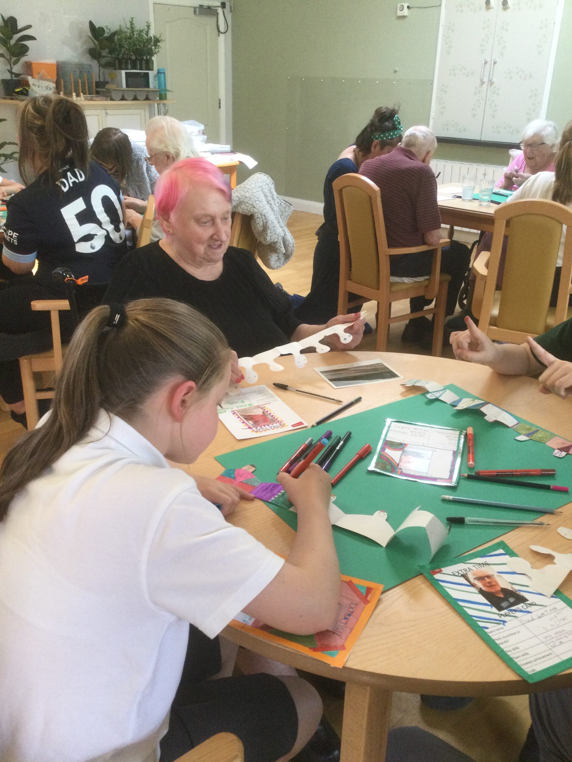 A room full of school children and adults, using pens to decorate rows of paper spectators