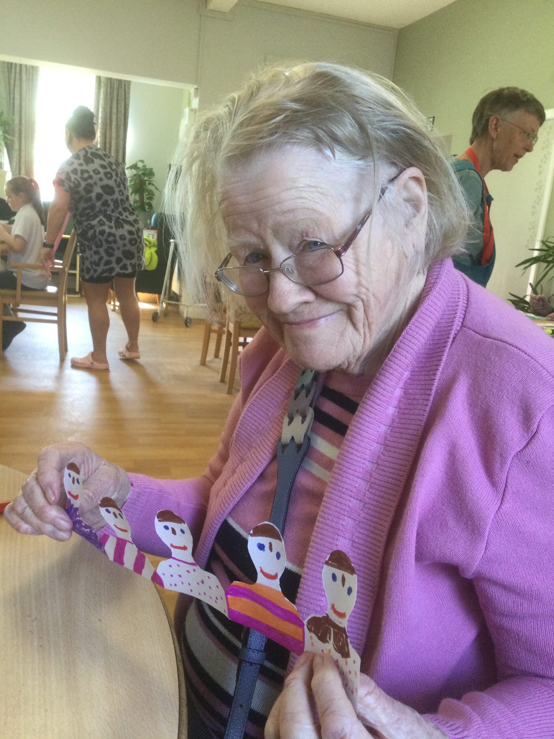 A woman wearing a pink cardigan holds up a row of decorated paper spectators