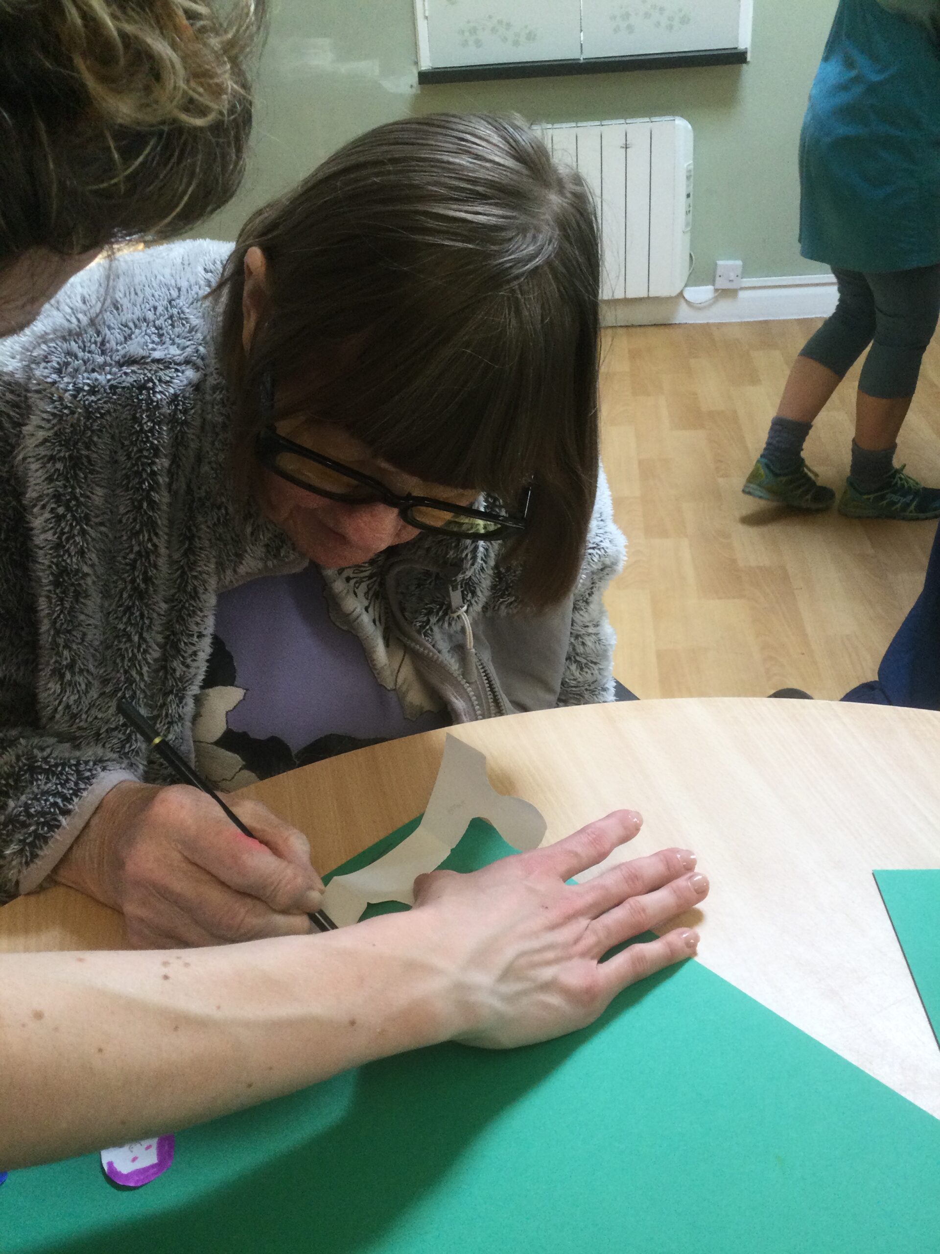 A hand holds a strip of paper flat whilst a woman draws on it