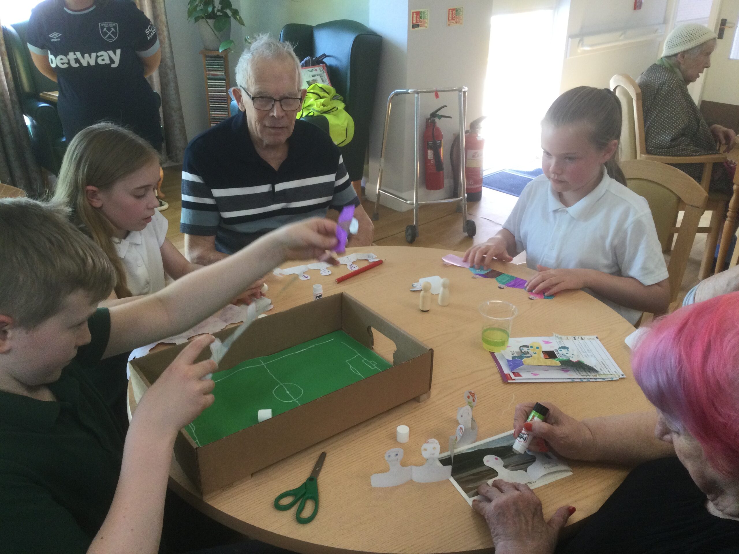 A group of children and adults sticking paper figures to the sides of a box